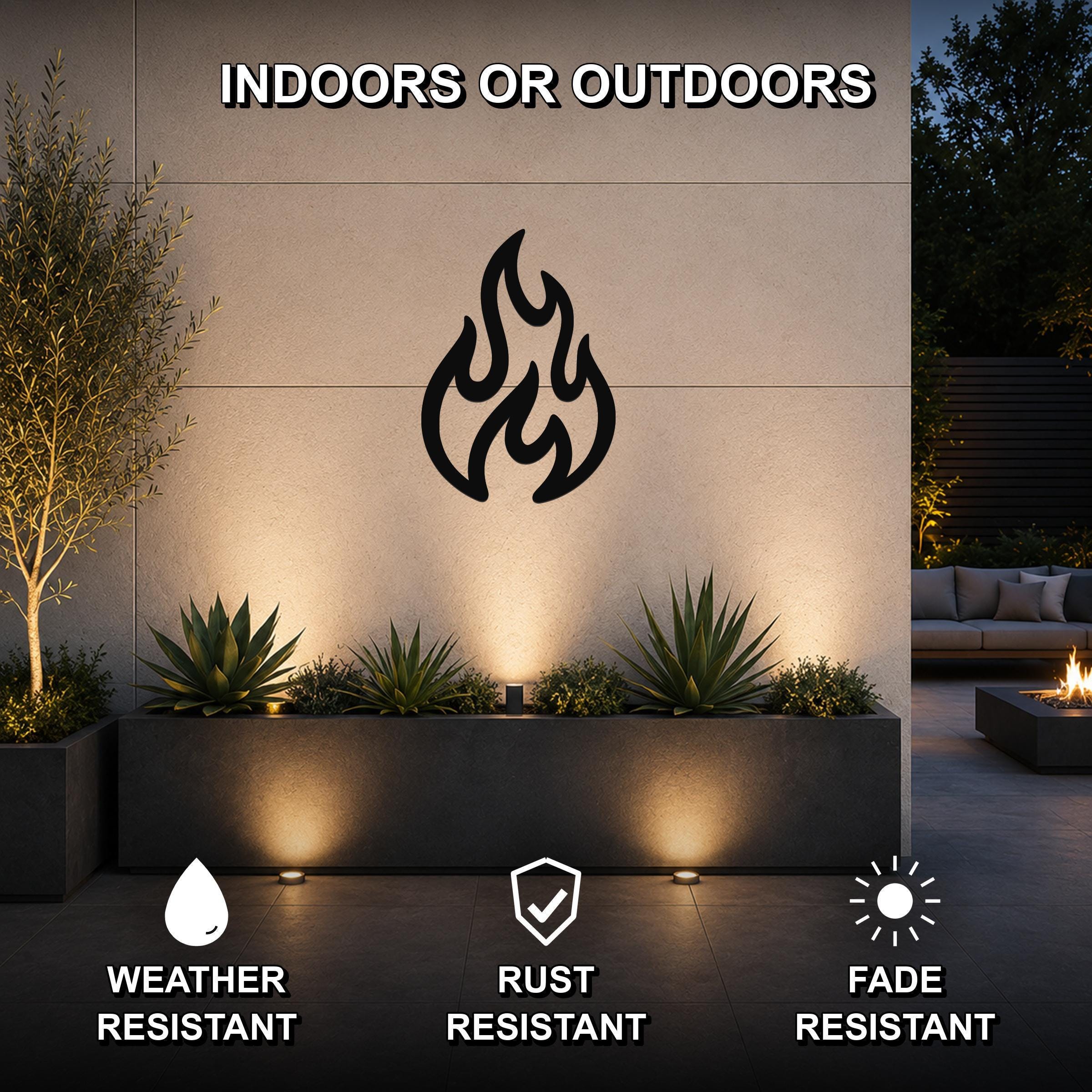 Black metal flame wall art with flowing cutout design, mounted on an outdoor wall above a planter in a modern patio setting.