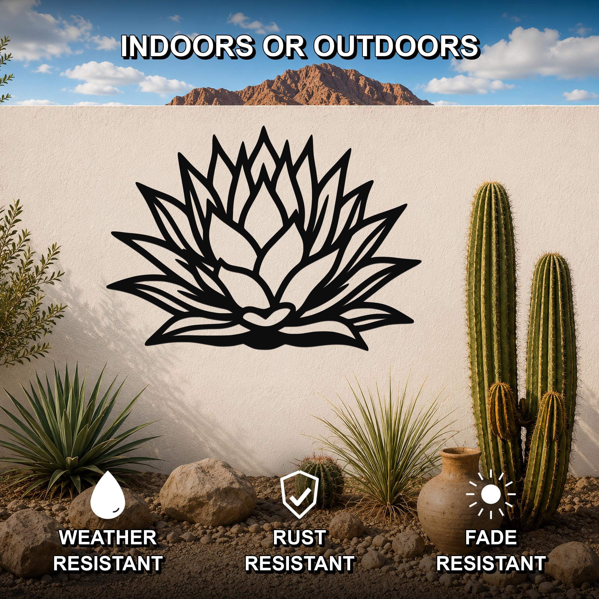 Black metal agave wall sculpture with leaf cutouts, mounted on a white outdoor wall in a desert garden setting.