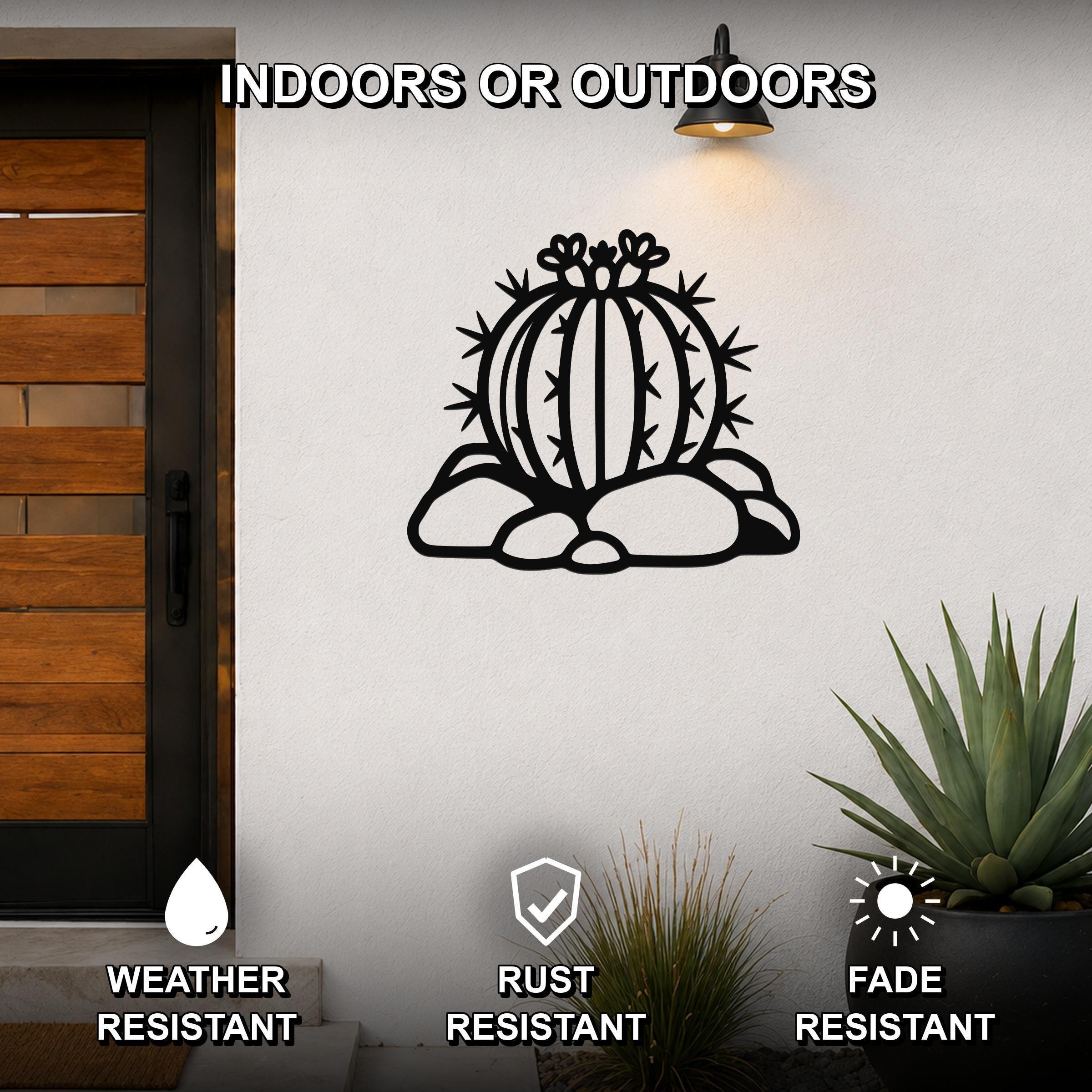 Black metal barrel cactus wall art with spines and flower cutouts, mounted on a white outdoor wall beside a wooden door.