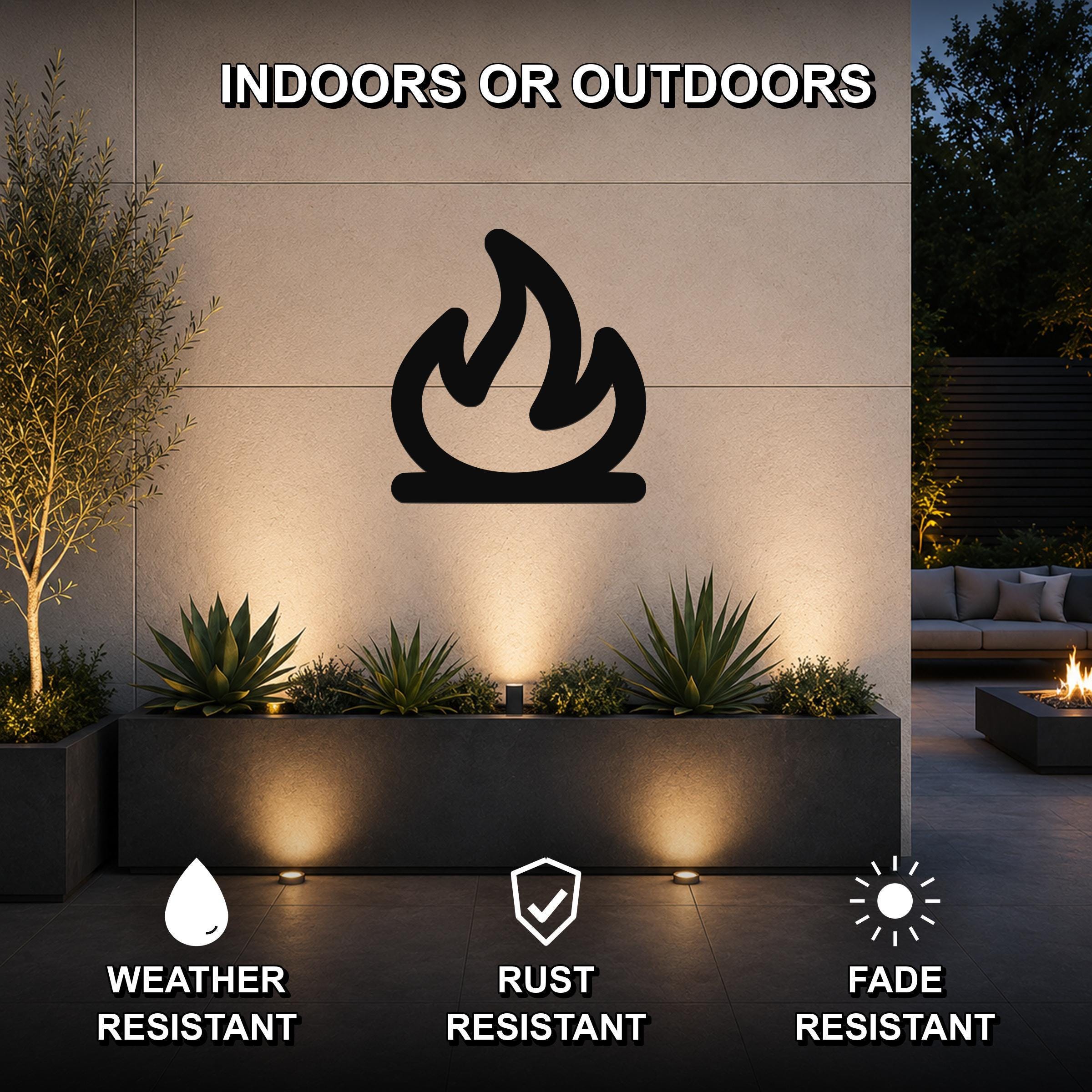 Black metal campfire silhouette wall art mounted on an outdoor wall above a planter, with warm lighting and visible weather, rust, and fade resistance icons.