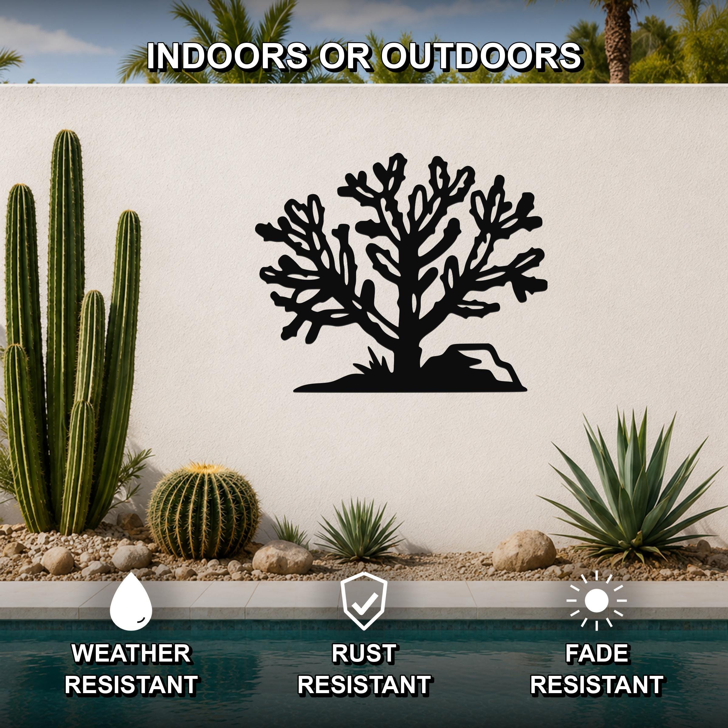 Black metal Cholla cactus wall art with intricate branch cutouts, mounted on a white outdoor wall above a pool in a desert garden setting.