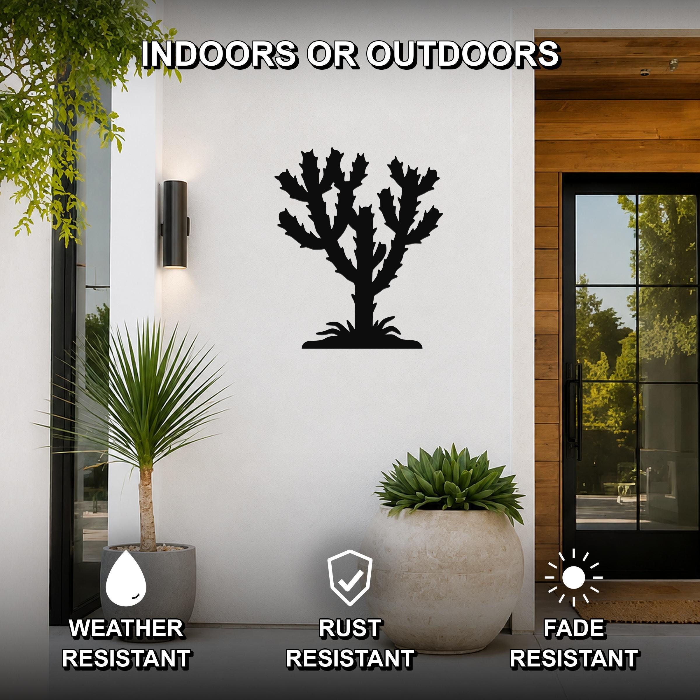 Black metal cholla cactus wall art silhouette mounted on a white exterior wall beside a glass door, with potted plants nearby and text indicating it is weather, rust, and fade resistant for indoor or outdoor use.