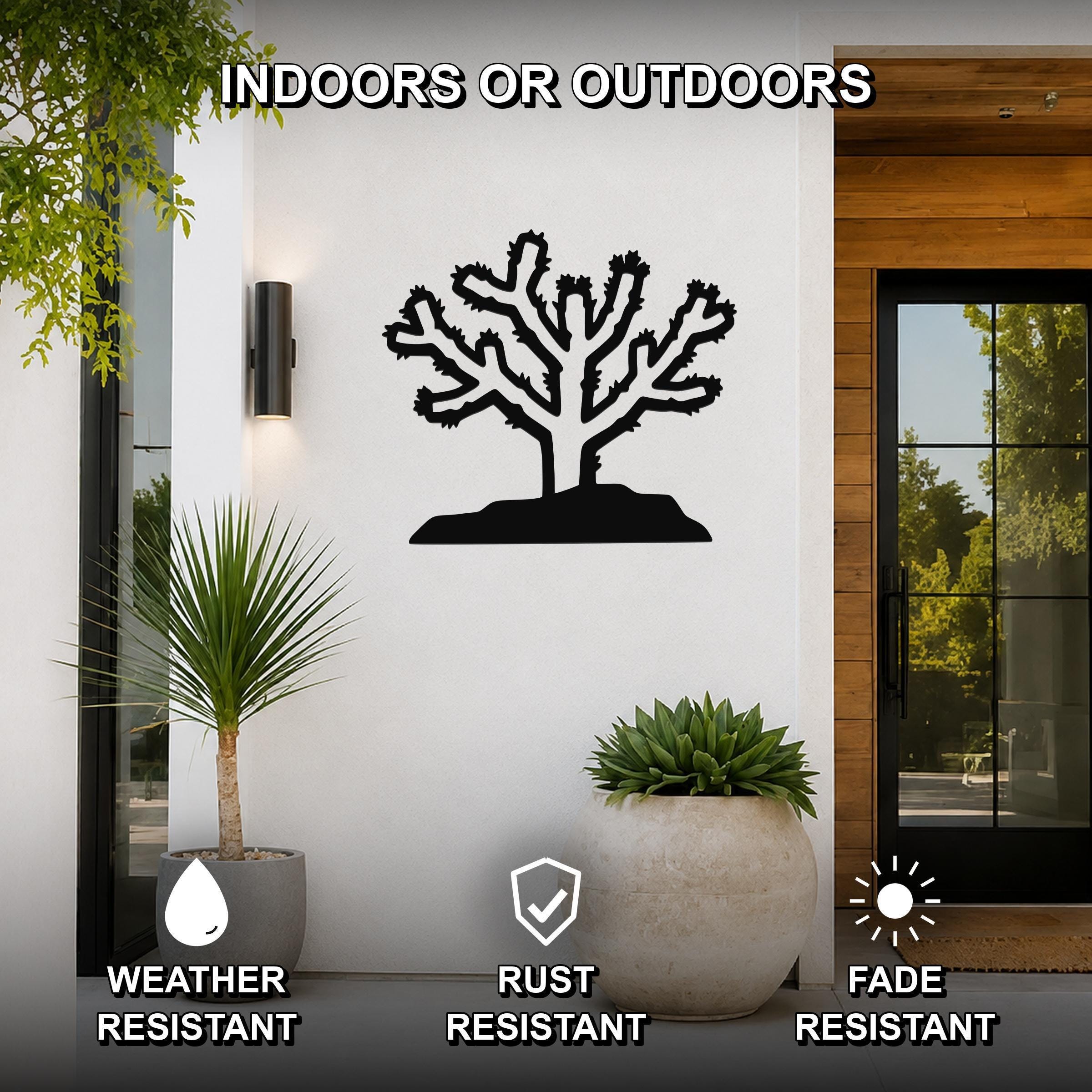 Black metal Cholla cactus wall art with branching silhouette, mounted on a white exterior wall beside a glass door and potted plants.