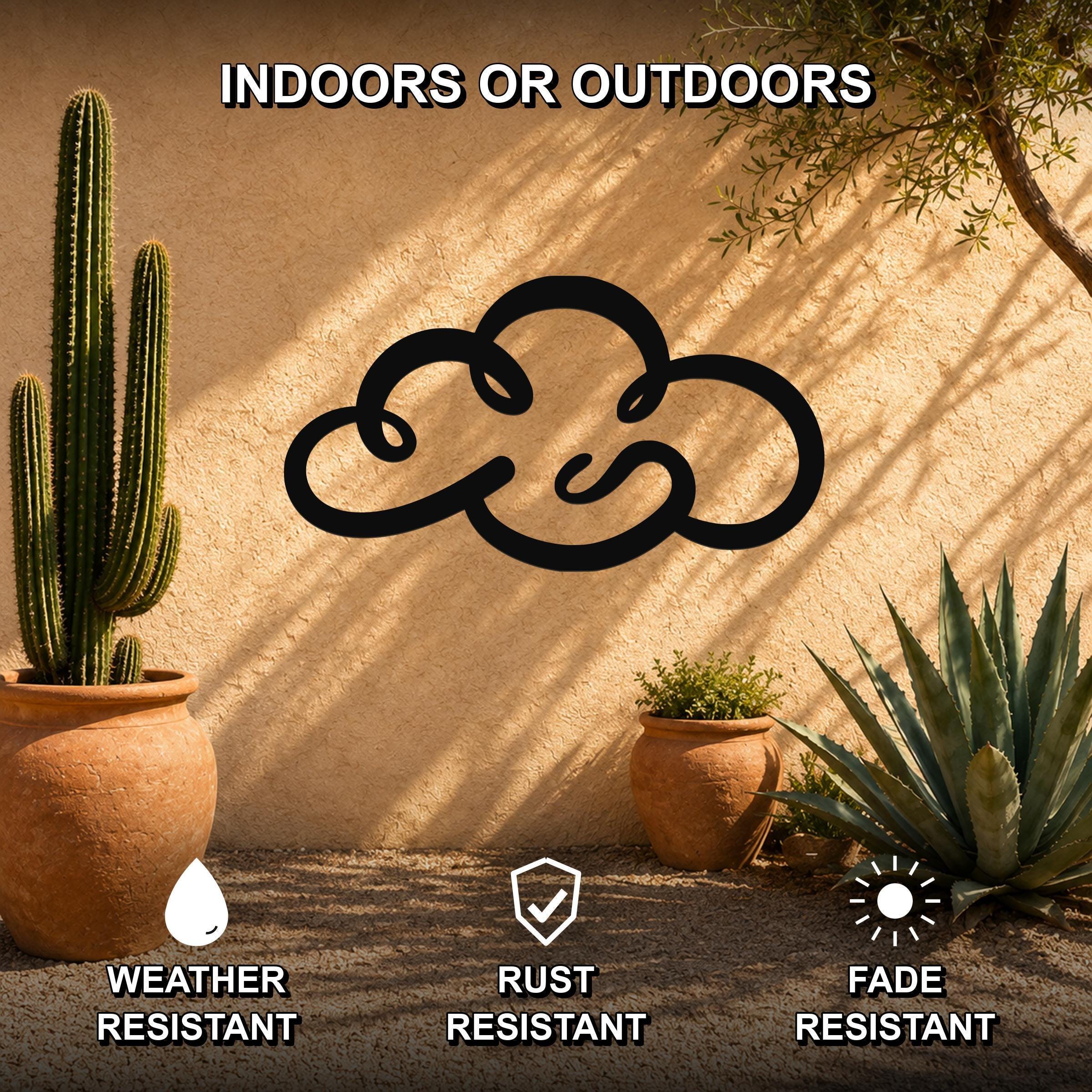 Black metal cloud wall art with a cutout silhouette, mounted on a stucco outdoor wall among potted cacti and succulents.