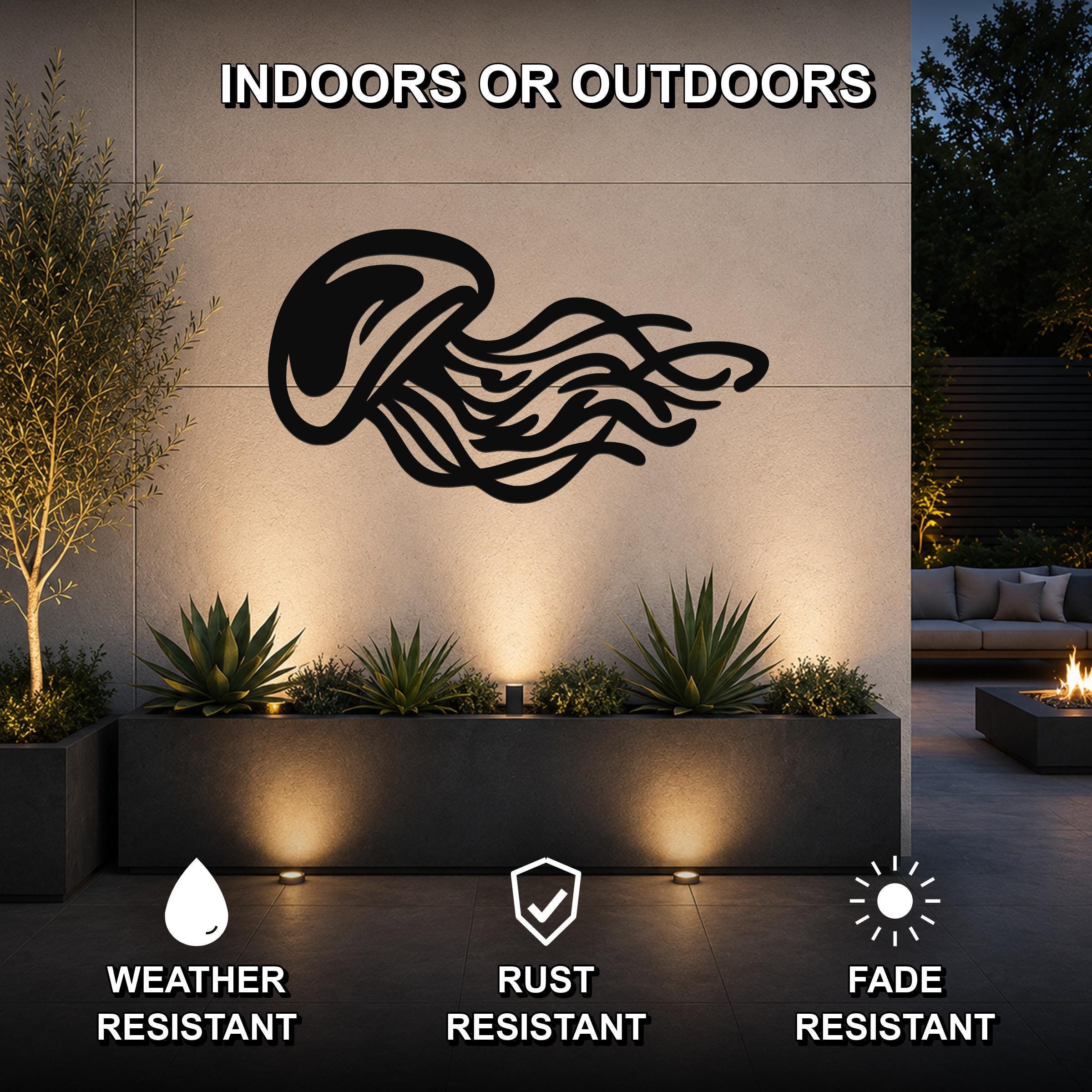 Black metal jellyfish wall art with flowing tentacle cutouts, mounted on an outdoor wall above a planter in a modern patio setting.