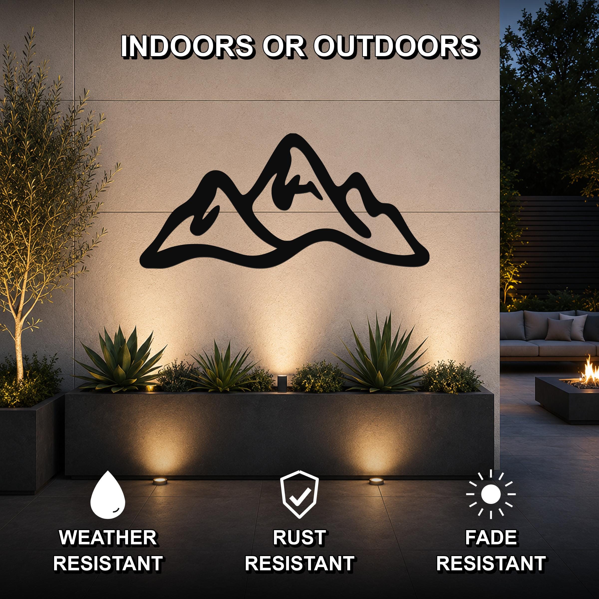 Black metal mountain range wall art with a silhouette design, mounted on an outdoor wall above a planter in a patio setting.