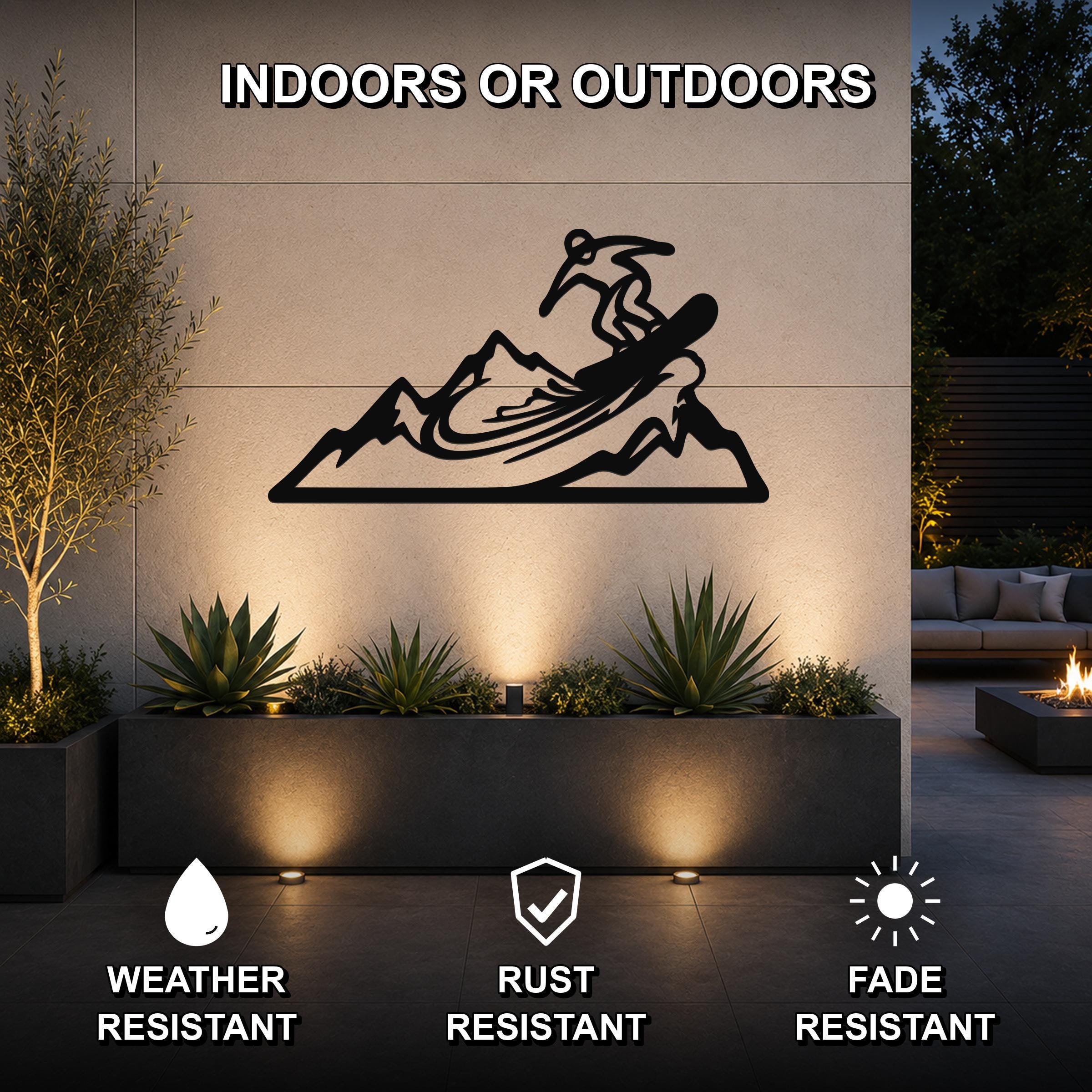 Black metal wall art featuring a snowboarder silhouette on a mountain, mounted on an outdoor wall above a planter in a patio setting.