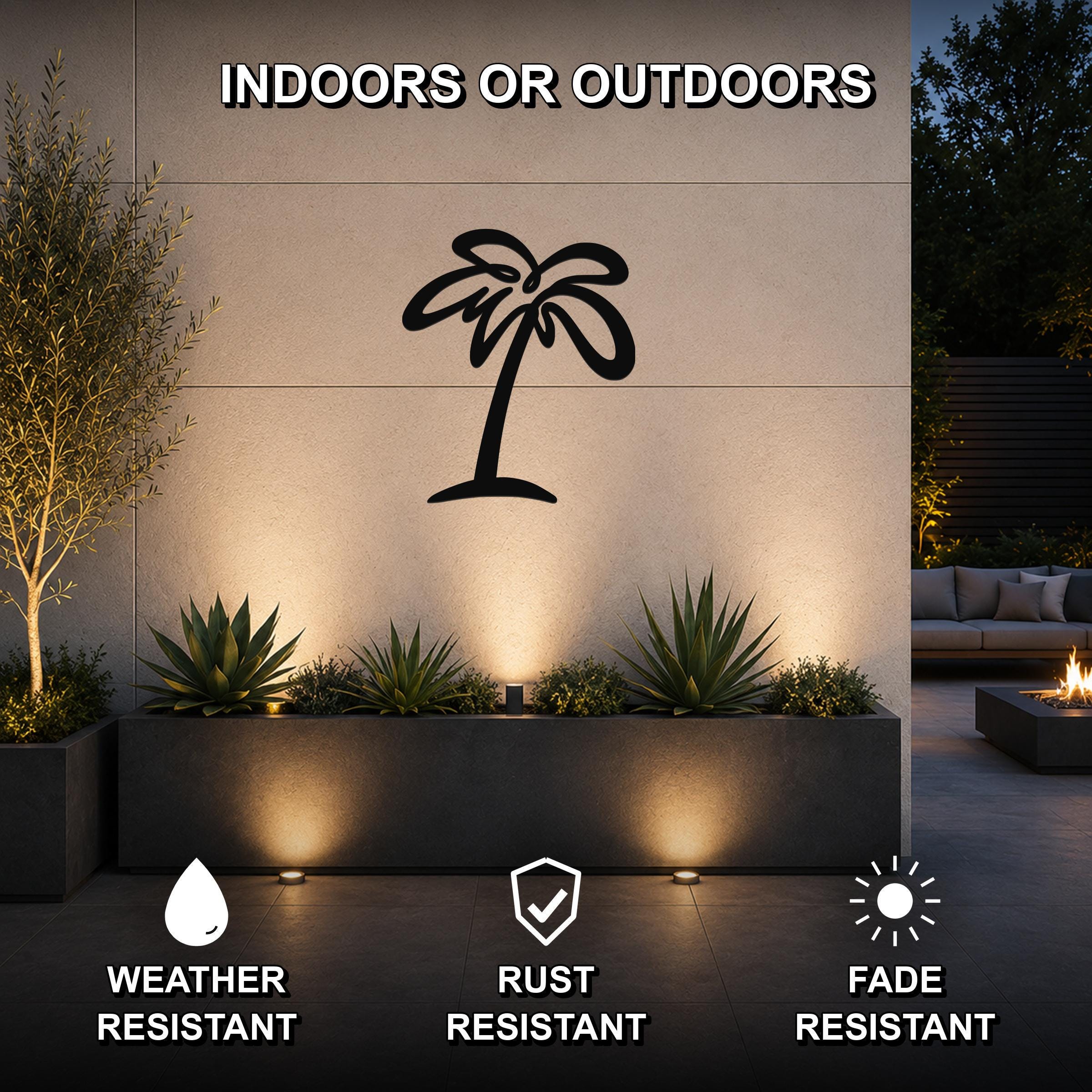 Black metal palm tree wall art silhouette mounted on an outdoor wall above a planter, illuminated by uplights in a patio setting.