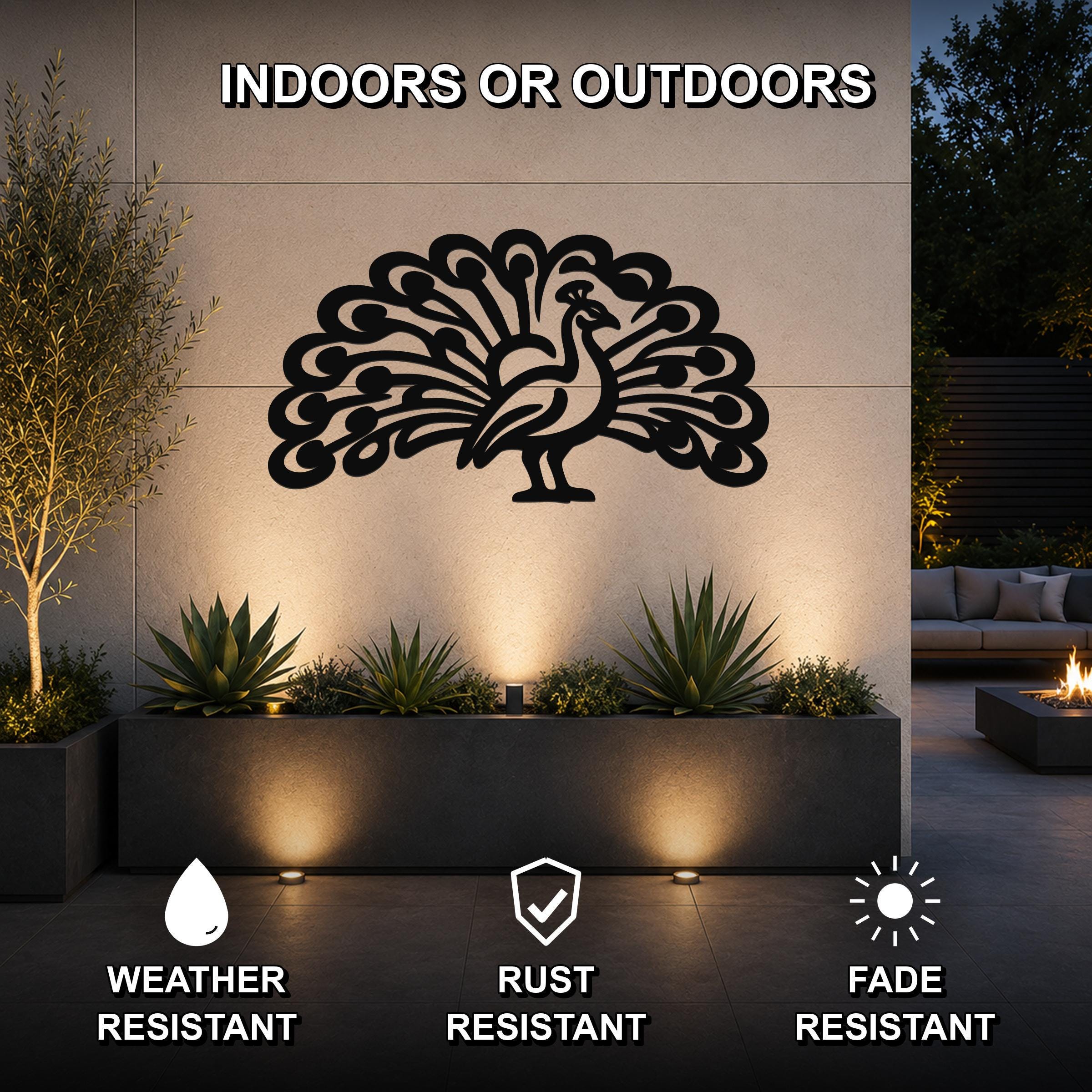 Black metal peacock wall art with intricate feather cutouts, mounted on an outdoor wall above a planter in a modern patio setting.