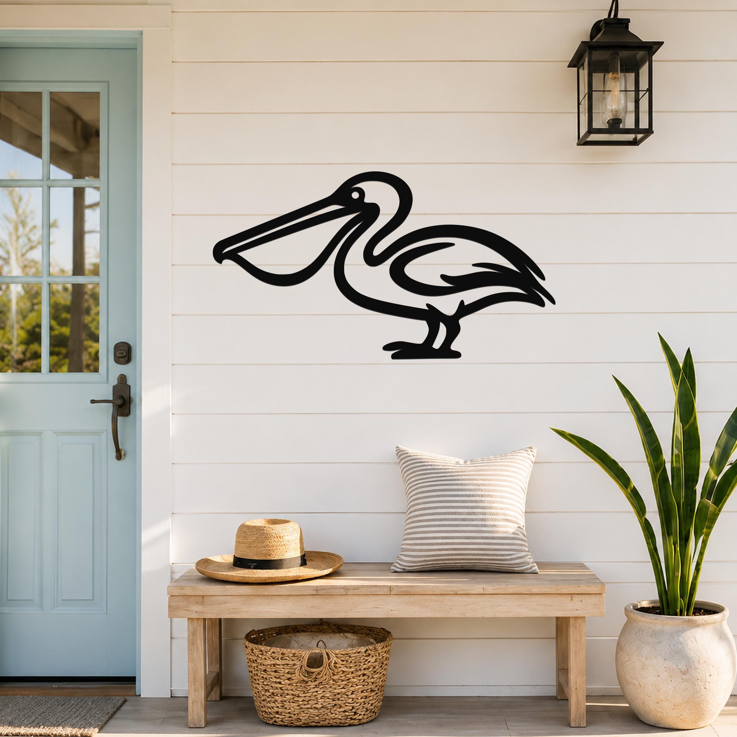 Black metal pelican wall art silhouette mounted on a white shiplap wall above a wooden bench in a coastal entryway.