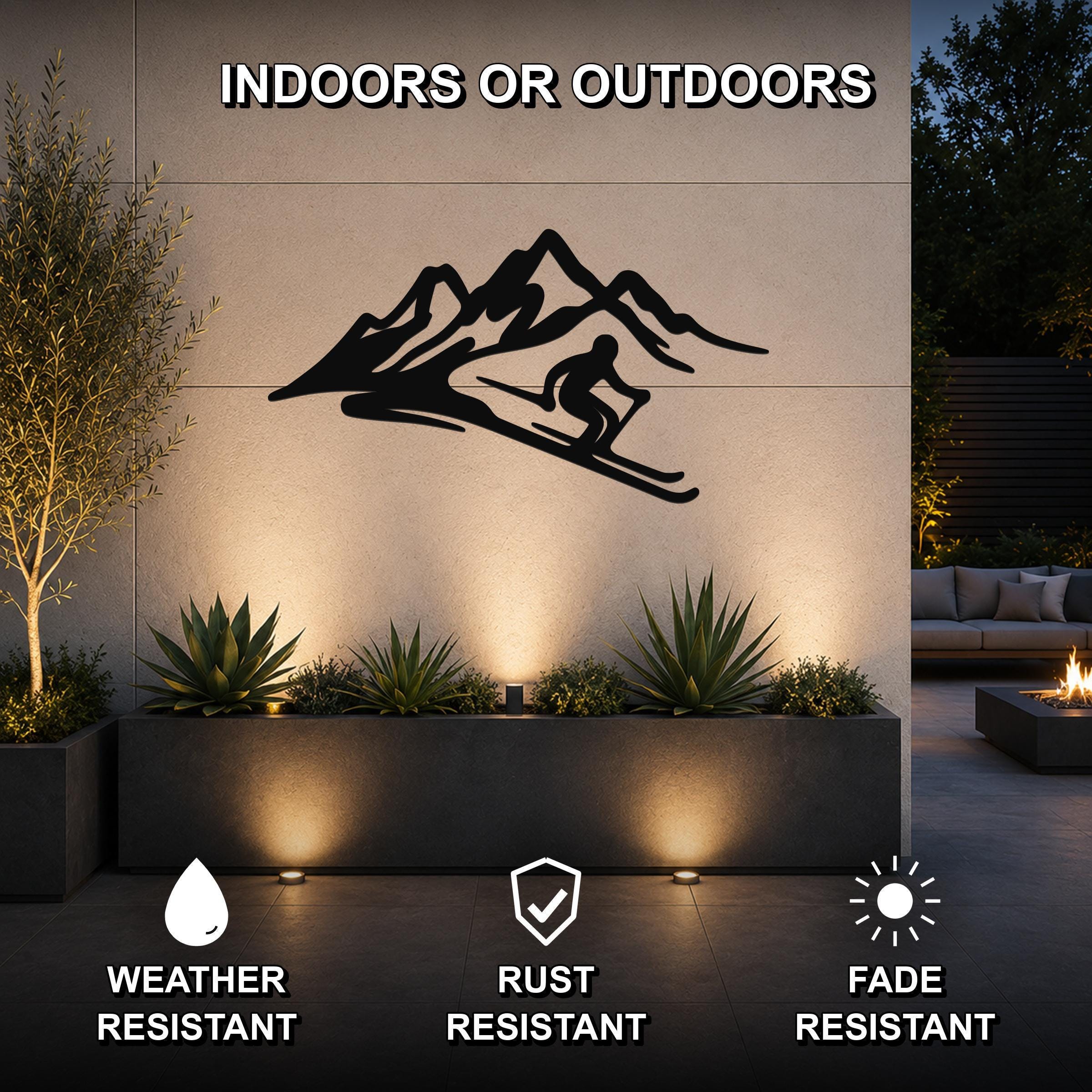 Black metal skier and mountain wall art with fluid motion cutouts, mounted on an outdoor patio wall above a planter with uplighting.