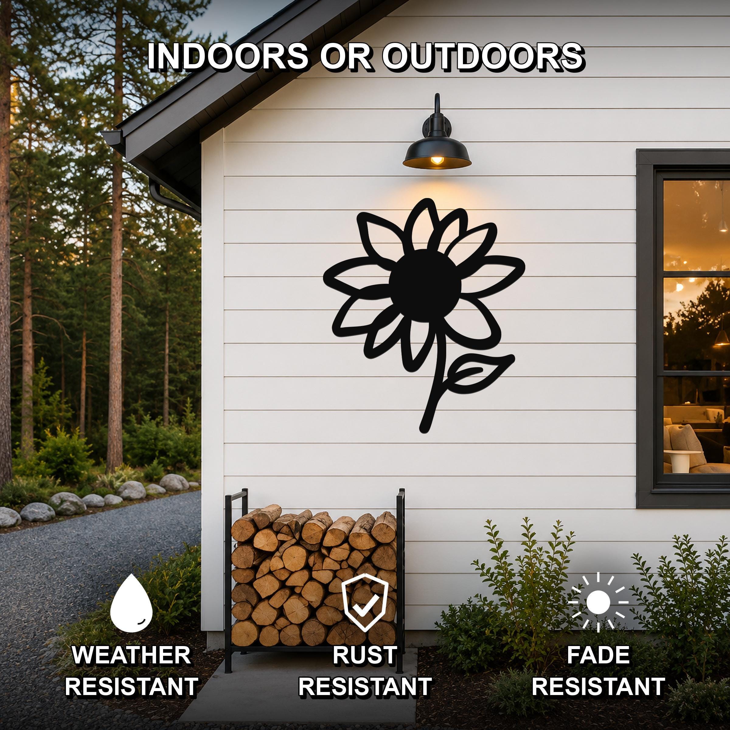 Black metal sunflower wall art with a bold silhouette design, mounted on a white exterior wall above a firewood rack, showcasing its weather-resistant, rust-resistant, and fade-resistant features for indoor or outdoor use.