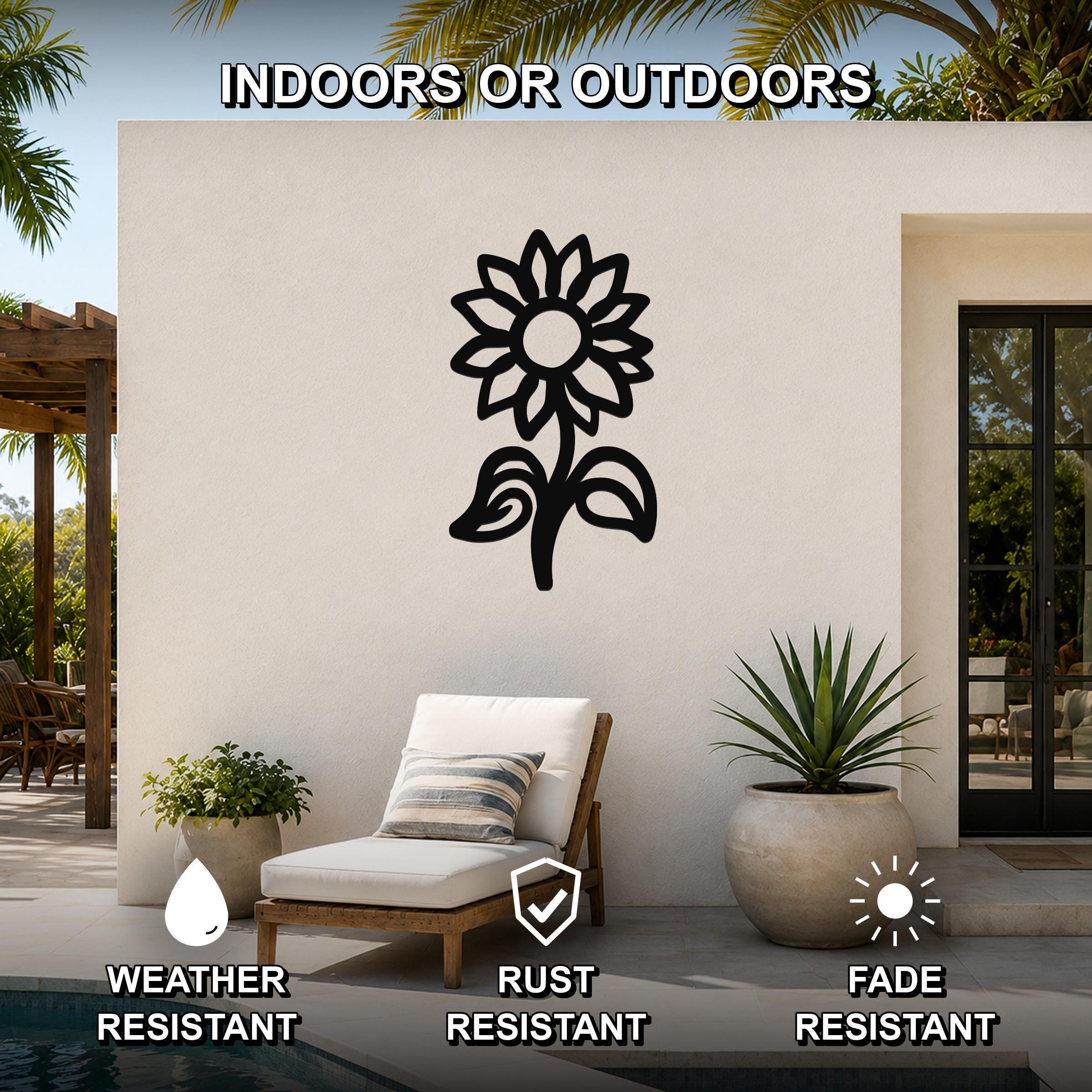 Black metal sunflower wall art with leaf and petal cutouts, mounted on an outdoor patio wall above a lounge chair.