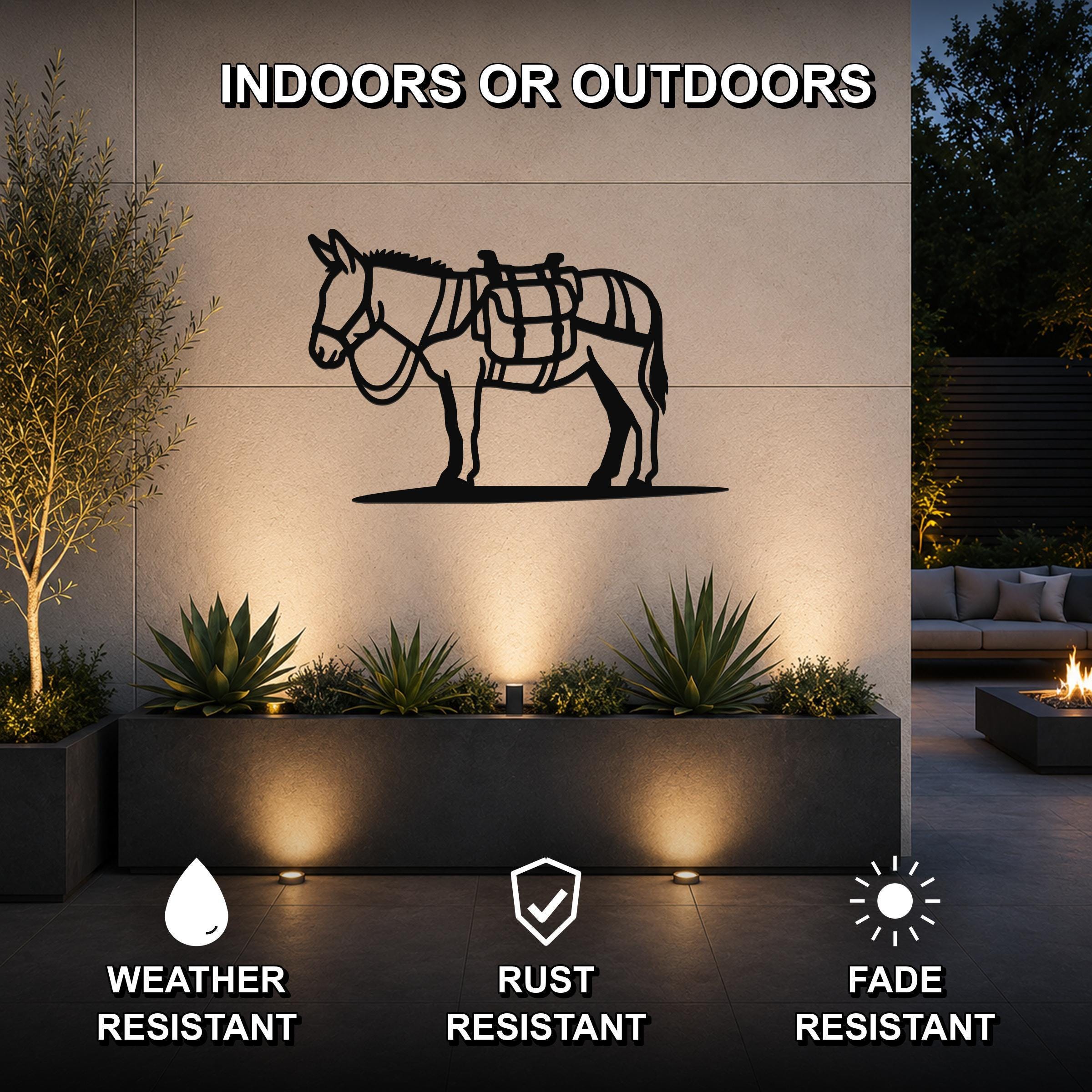 Black metal burro wall art with saddle cutouts, mounted on an outdoor wall above a planter in a patio setting.