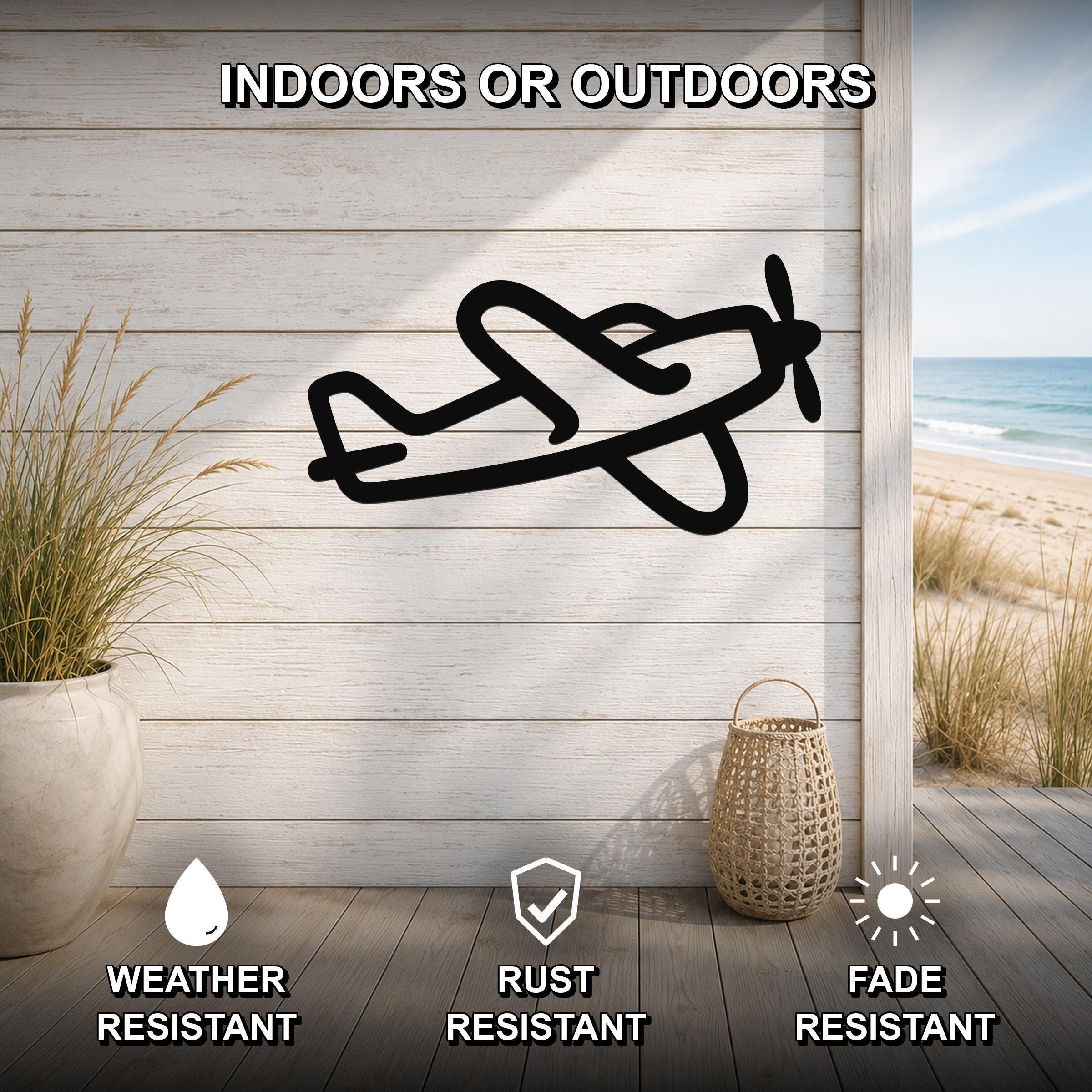 Black metal airplane wall art silhouette mounted on a light wood plank wall above a wooden deck, with a beach view visible through an opening.