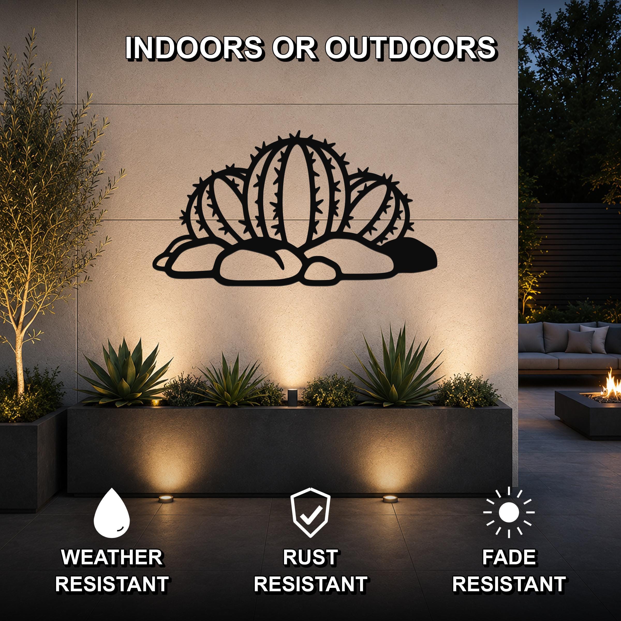 Black metal barrel cactus wall art with spines and rocks cutout, mounted on an outdoor wall above a planter in a patio setting.