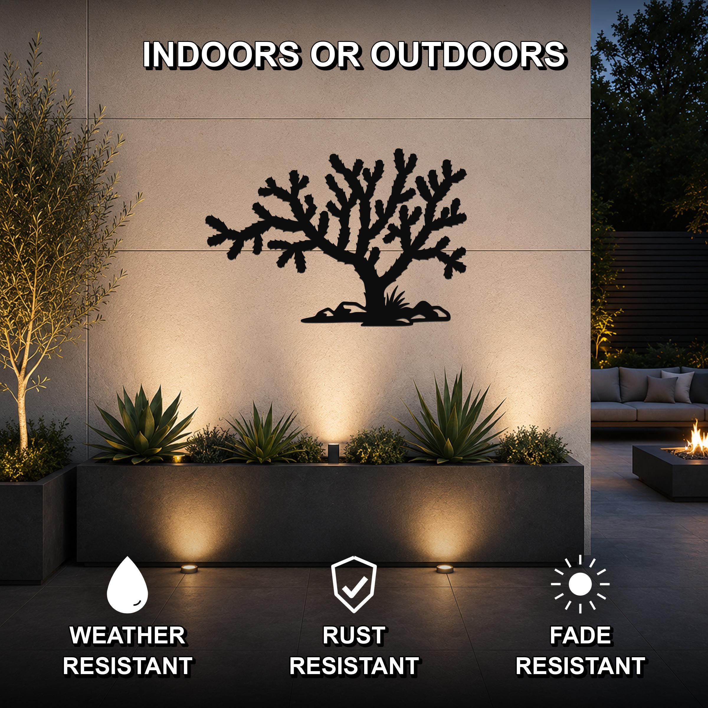 Black metal Cholla cactus wall art with branching silhouette, mounted on an outdoor wall above a planter in a patio setting.