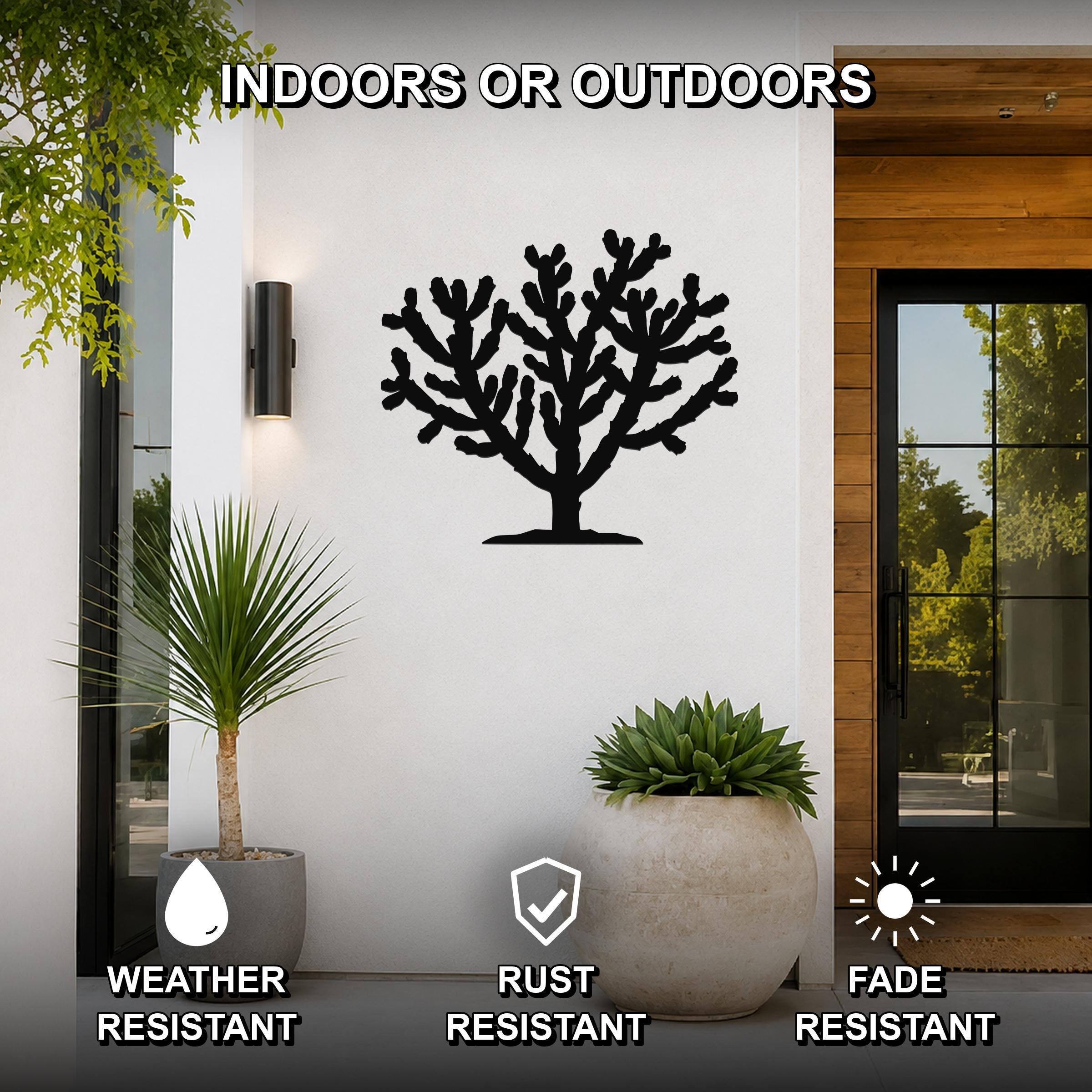 Black metal Cholla cactus wall art silhouette with branching cutouts, mounted on a white exterior wall beside a glass door and potted plants.