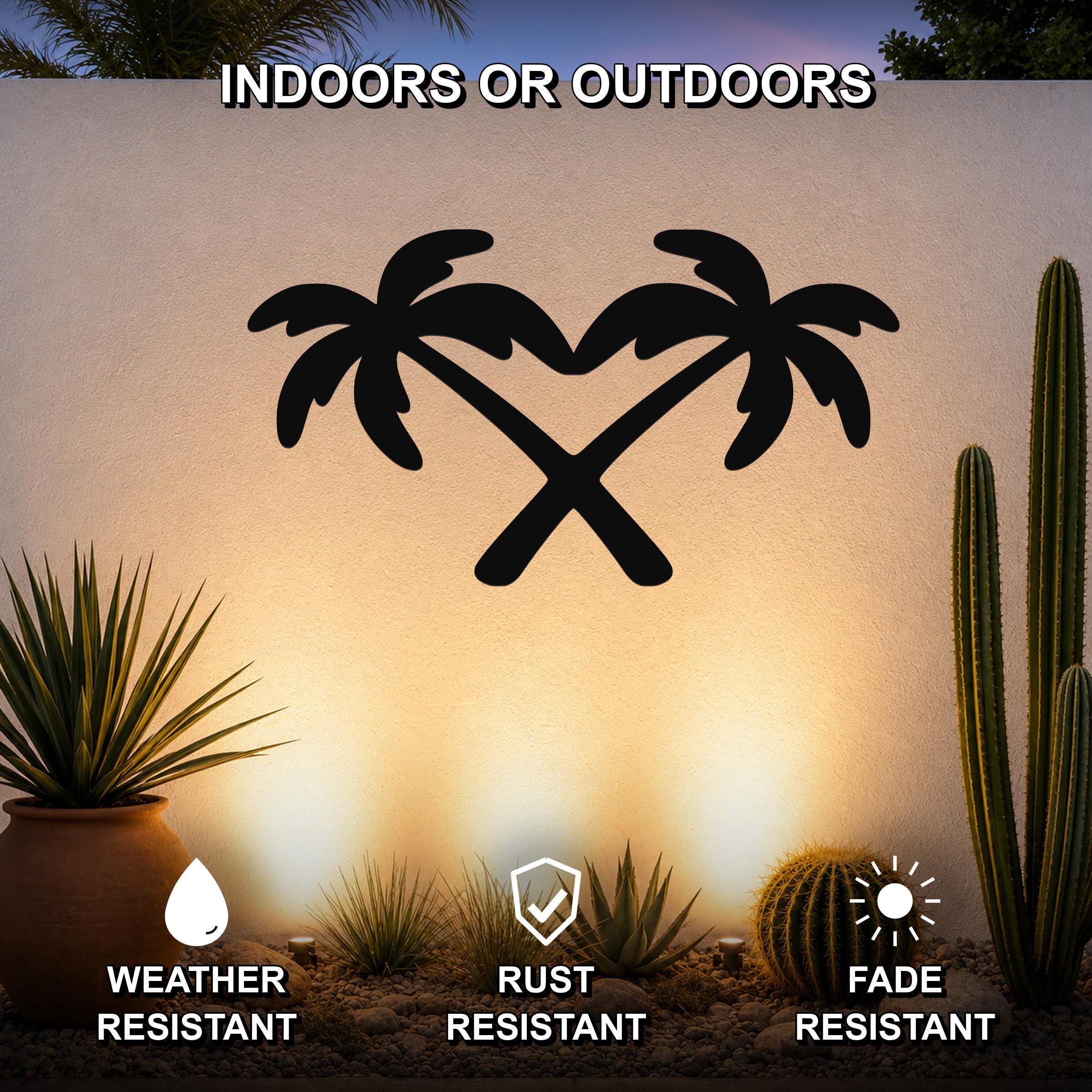 Black metal palm tree wall art with crossed trunks forming a heart shape, mounted on an outdoor wall above a desert garden with cacti and succulents.
