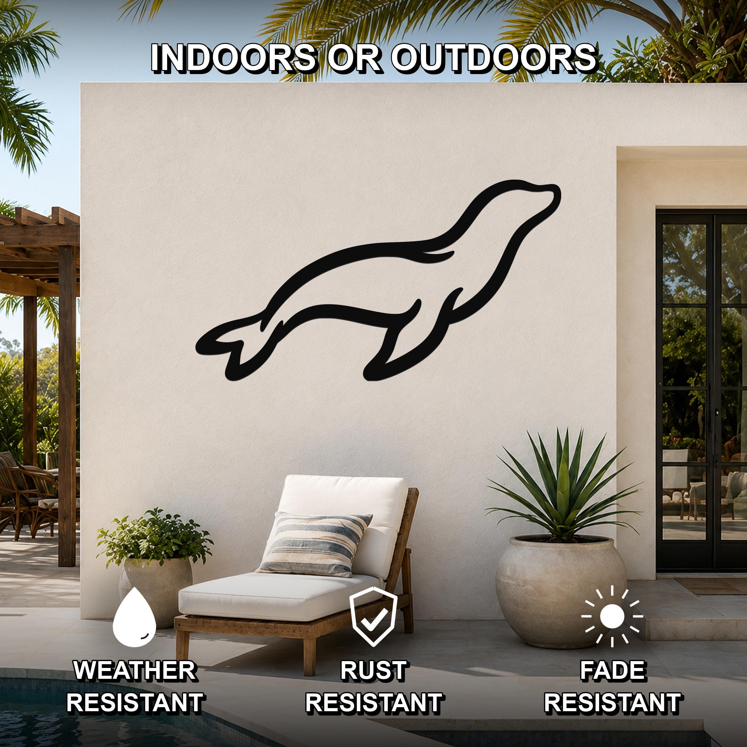 Black metal sea lion wall art with a sleek silhouette design, mounted on an outdoor patio wall above a lounge chair near a pool.