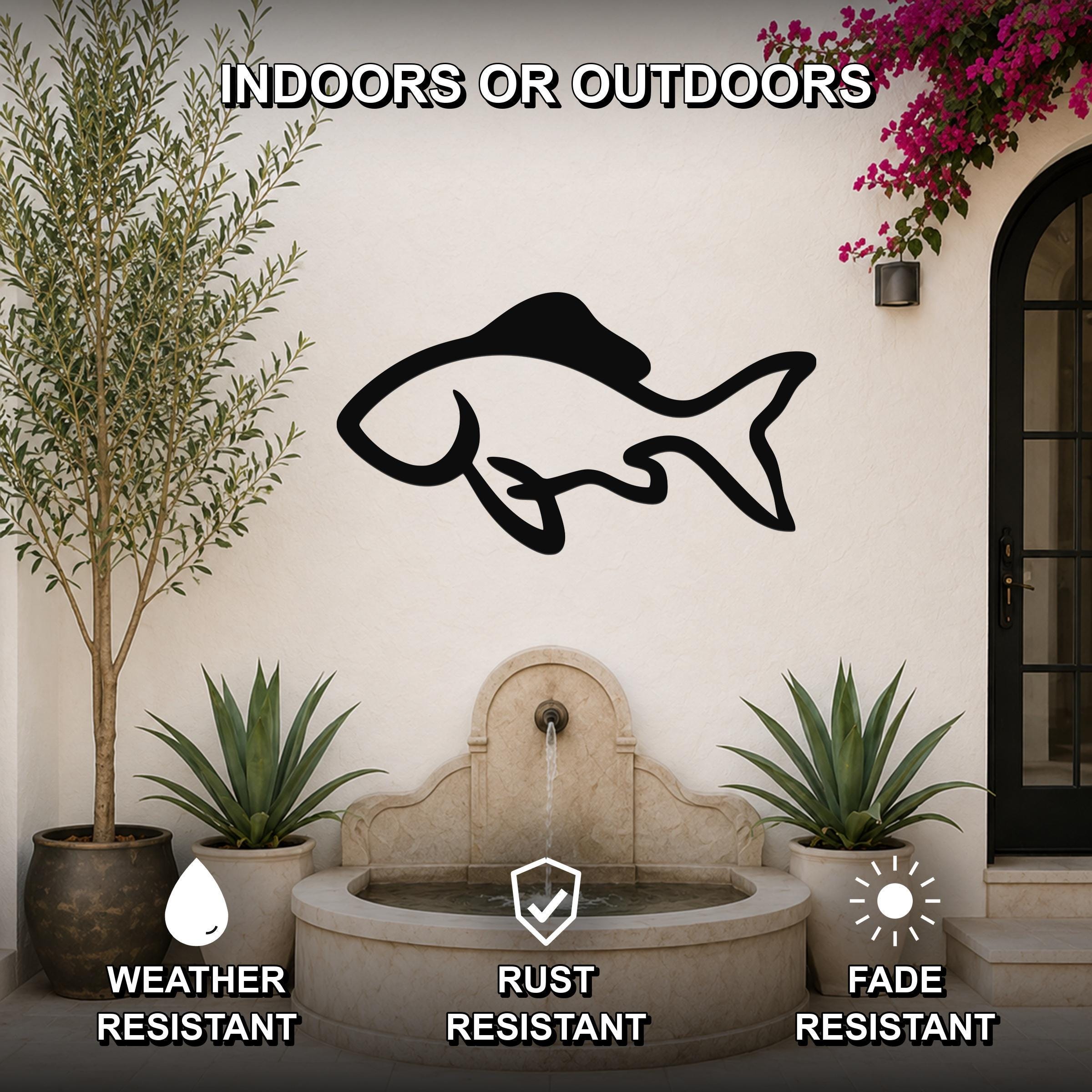 Black metal fish wall art with a silhouette design, mounted on an outdoor wall above a stone fountain, surrounded by potted plants and a flowering vine.