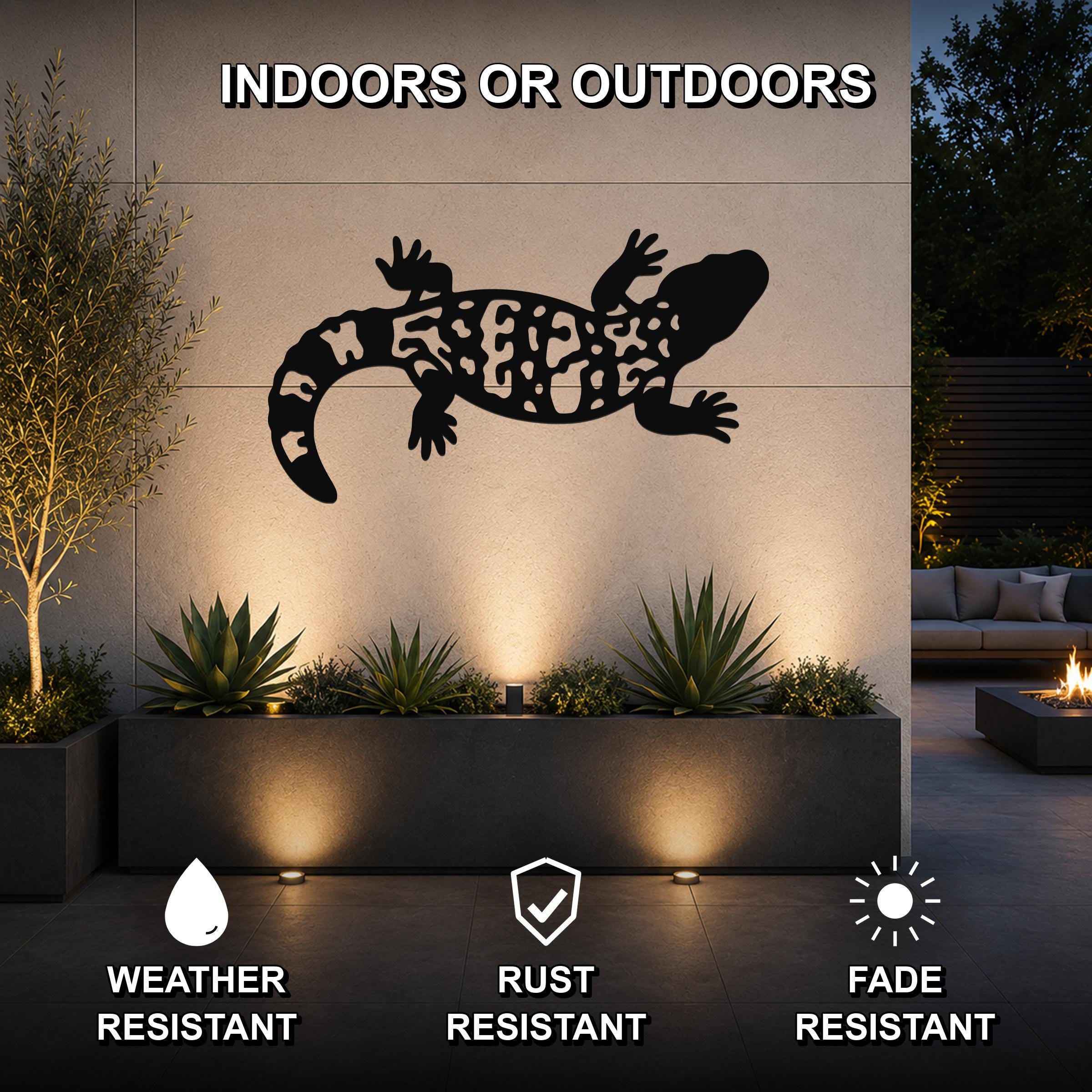 Black metal Gila monster wall art with intricate cutout patterns, mounted on an outdoor wall above a planter in a modern patio setting.
