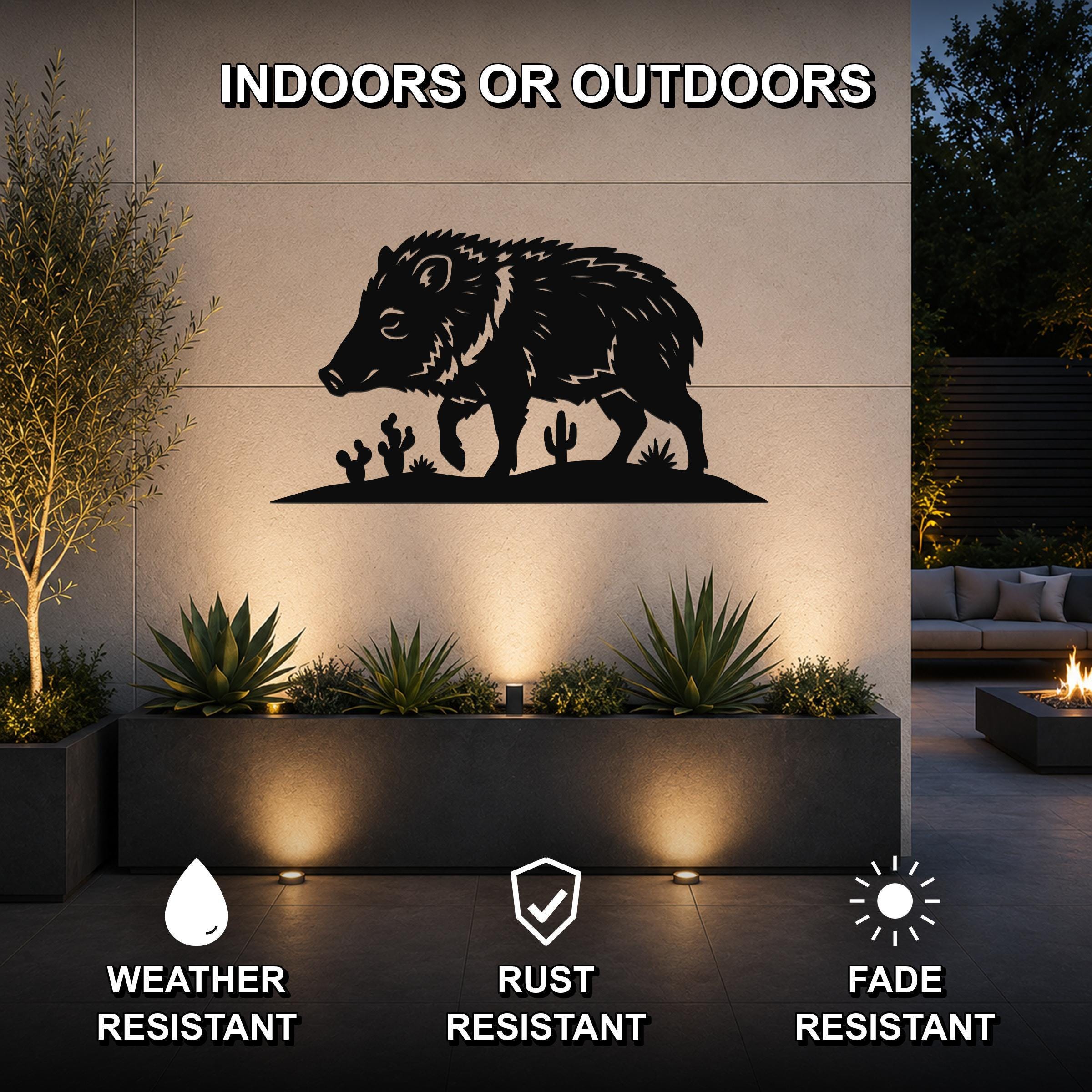 Black metal javelina wall art with cactus cutouts, mounted on an outdoor wall above a planter in a patio setting.