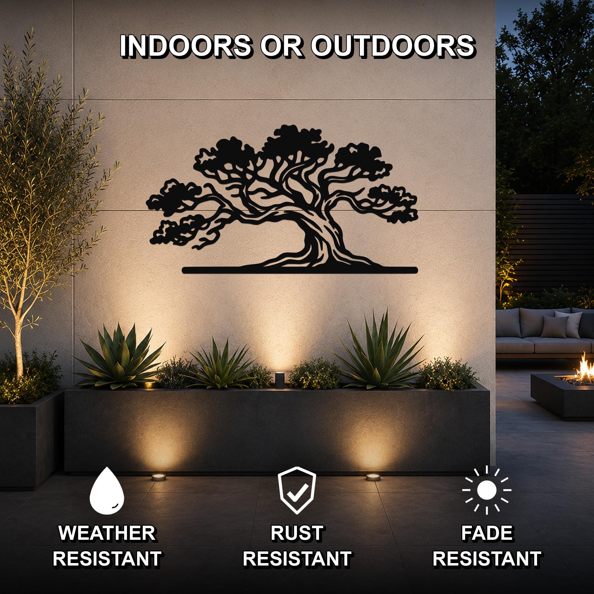 Black metal juniper tree wall art with intricate branch cutouts, mounted on an outdoor wall above a planter in a modern patio setting.