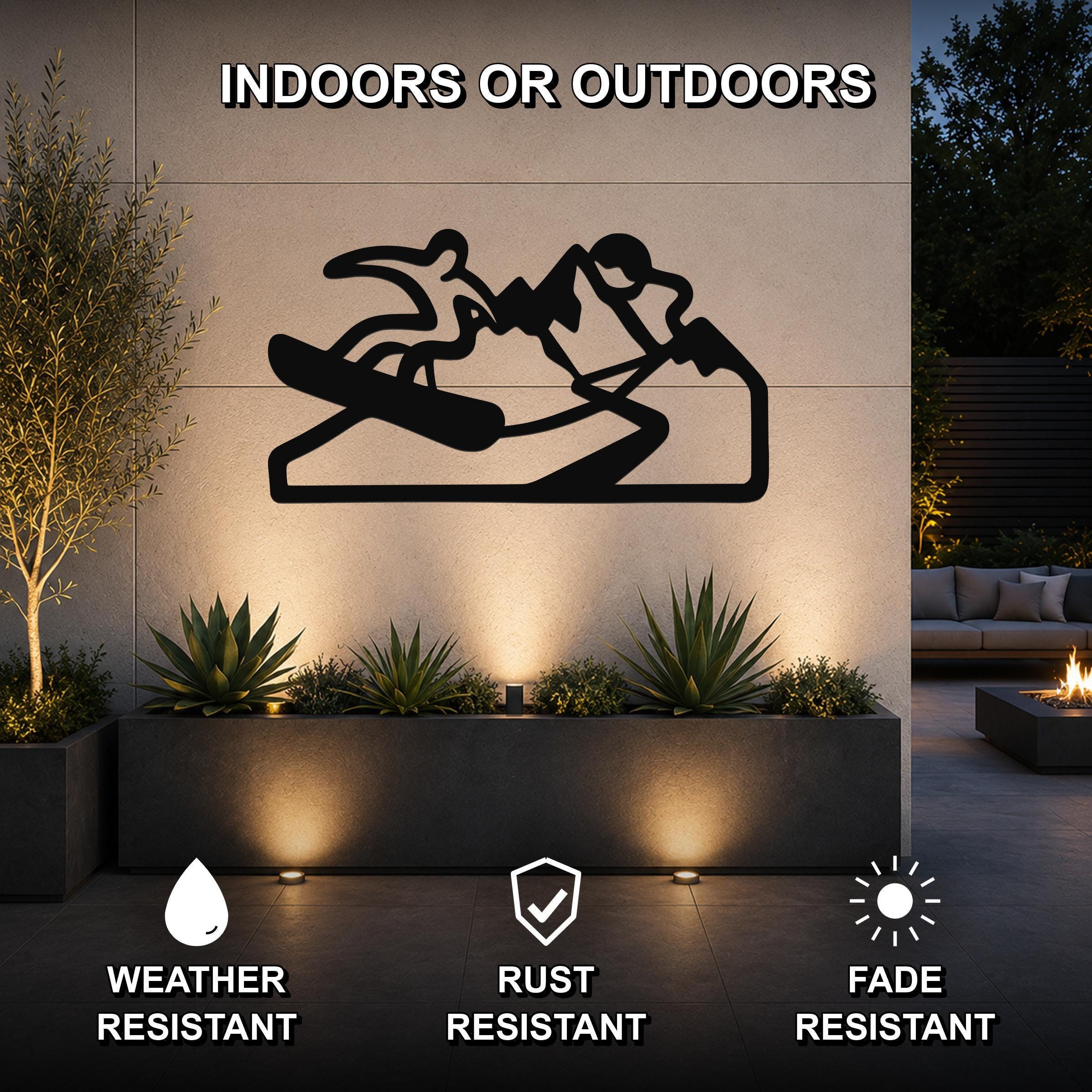 Black metal wall art silhouette of a snowboarder on a mountain, mounted on an outdoor wall above a planter in a patio setting.