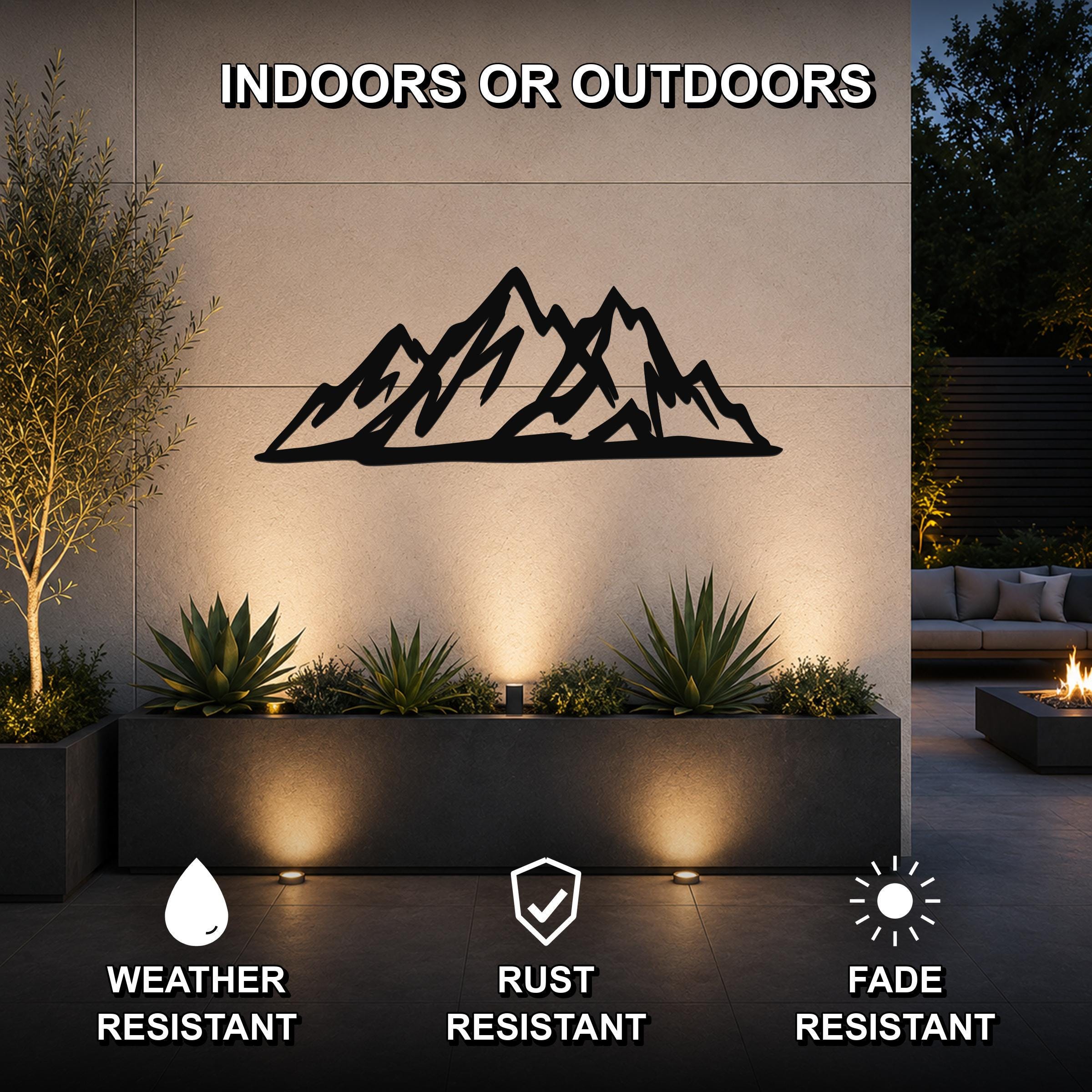 Black metal mountain silhouette wall art mounted on an outdoor wall above a planter, with visible cutout peaks and a modern rustic design.