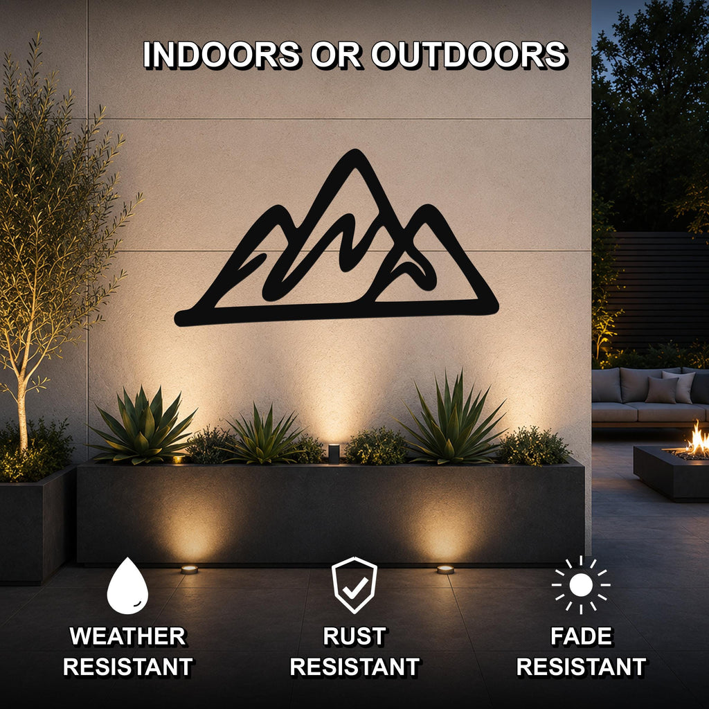 Black metal mountain silhouette wall art mounted on an outdoor wall above a planter, with text indicating it is weather, rust, and fade resistant.