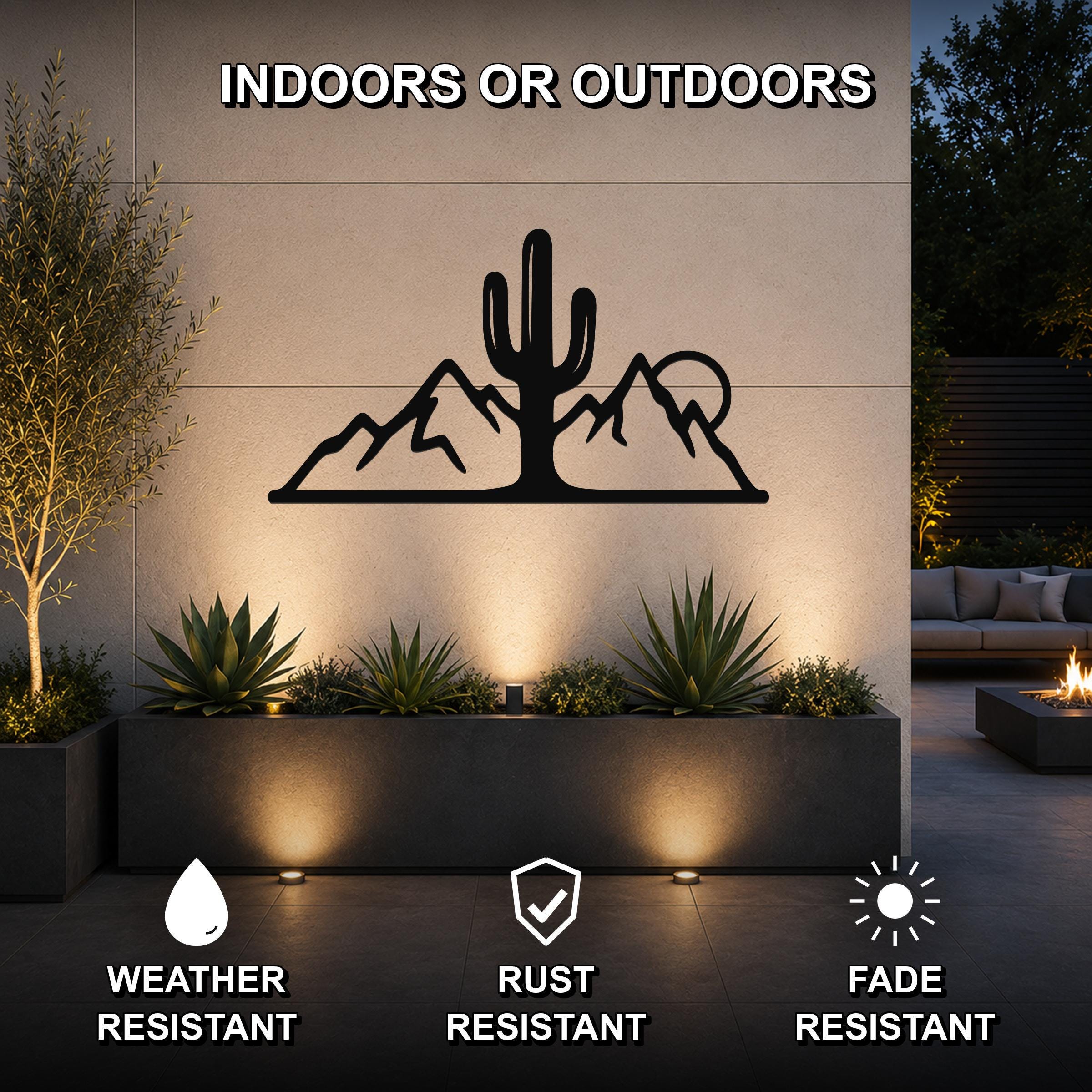 Black metal wall art featuring a saguaro cactus and mountain silhouette, mounted on an outdoor wall above a planter in a patio setting.