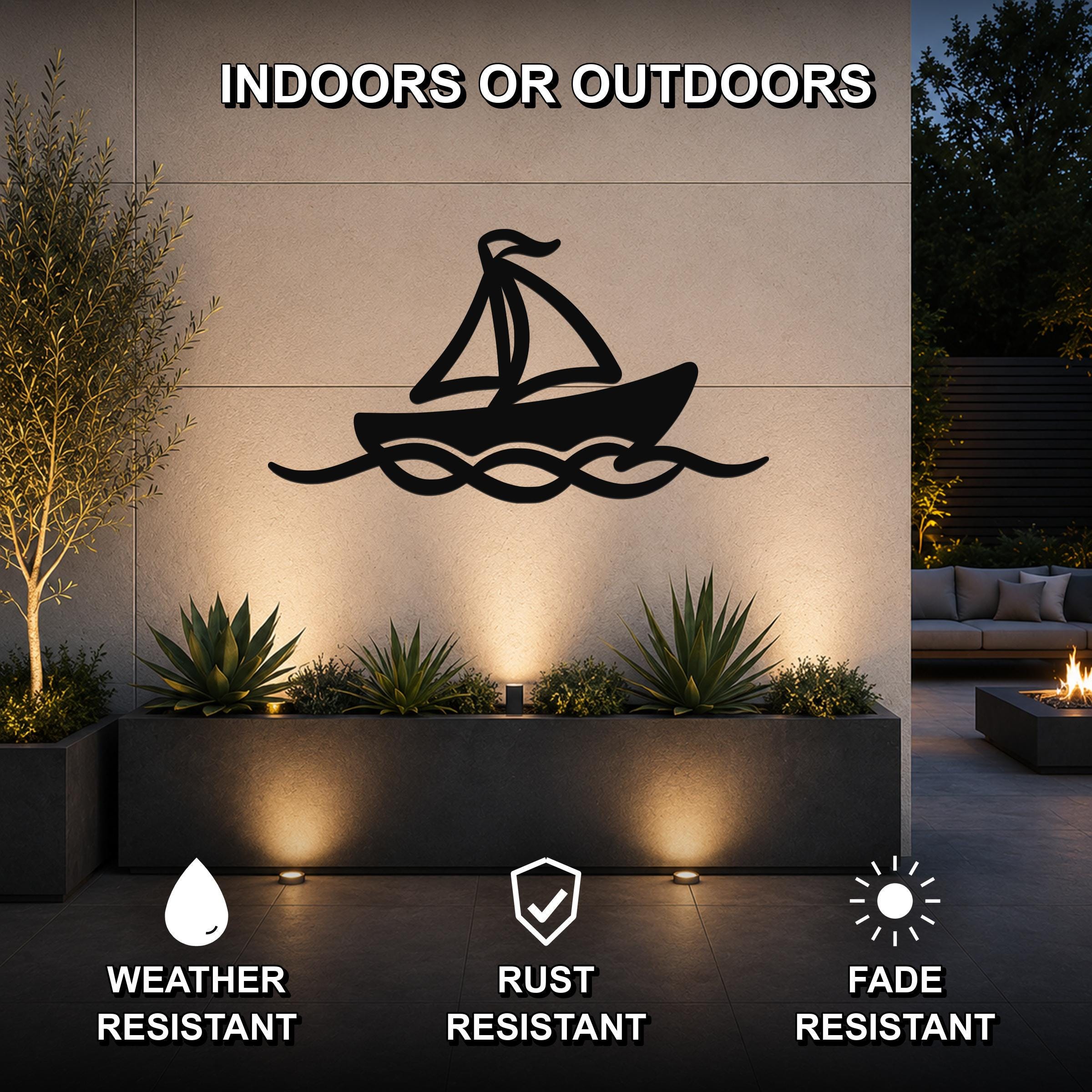 Black metal sailboat wall art with wave cutouts, mounted on an outdoor wall above a planter in a modern patio setting.