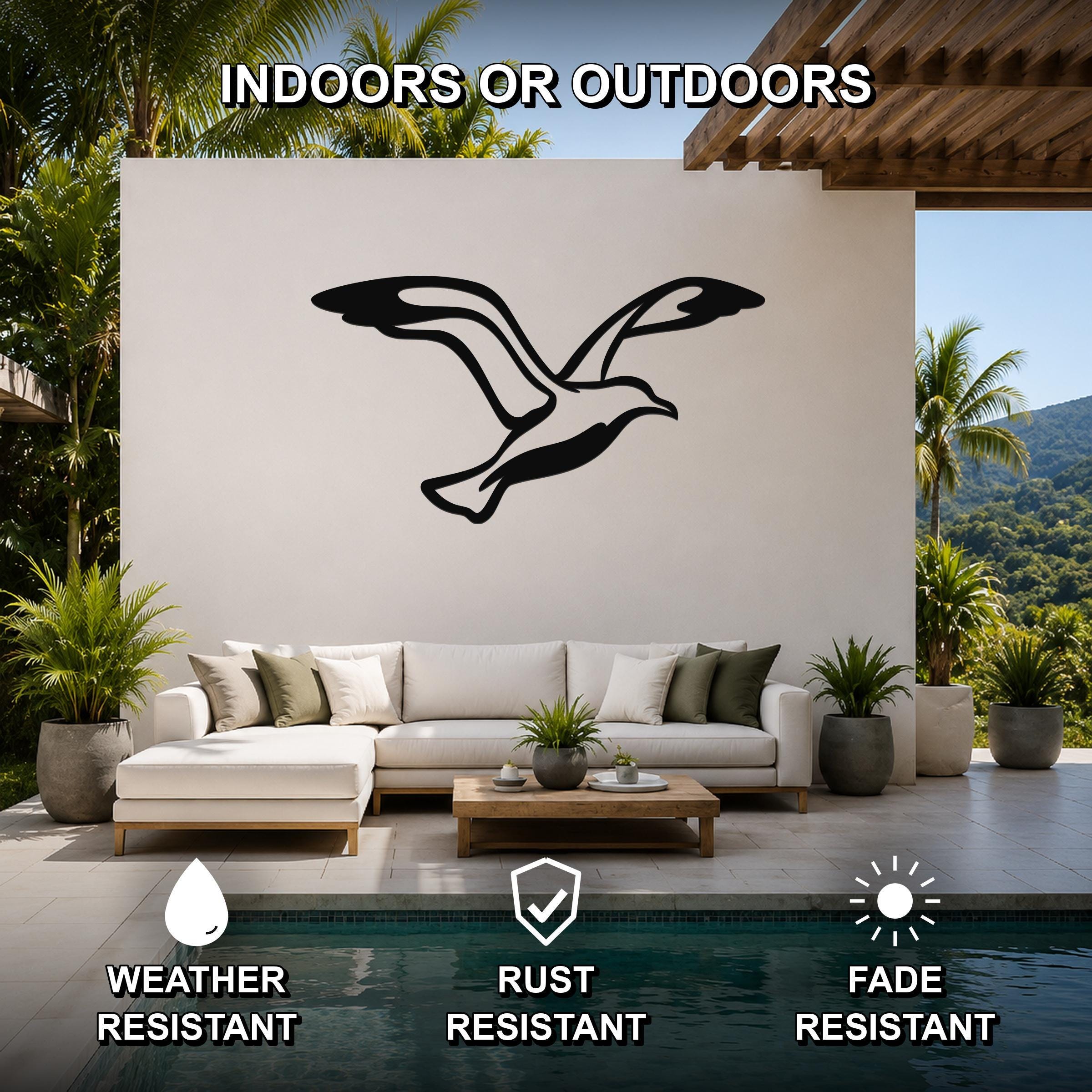 Black metal seagull wall art with wing and tail cutouts, mounted on a white outdoor wall above a sofa in a patio living area.