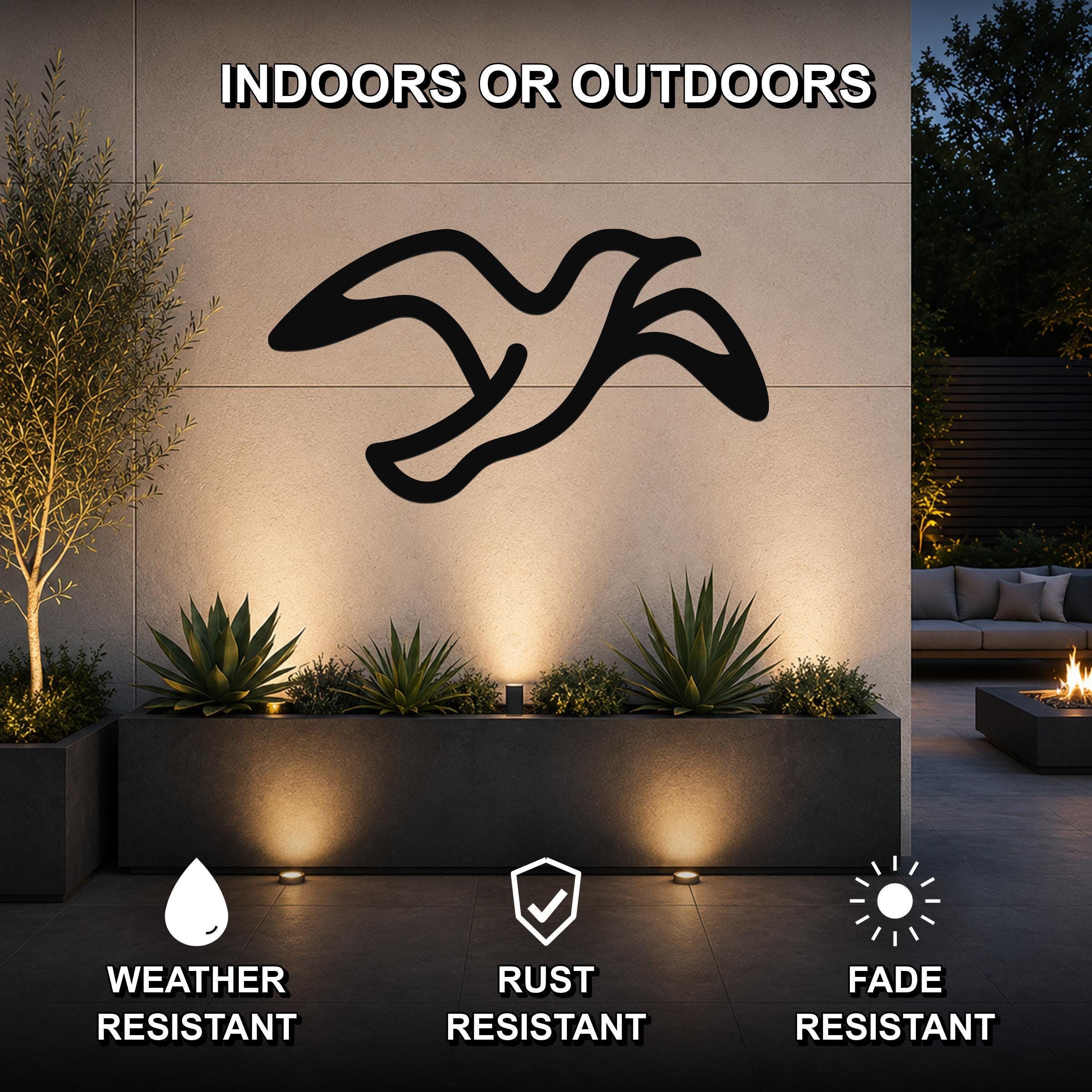 Black metal seagull wall art with motion-line cutouts, mounted on an outdoor wall above a planter in a patio setting.