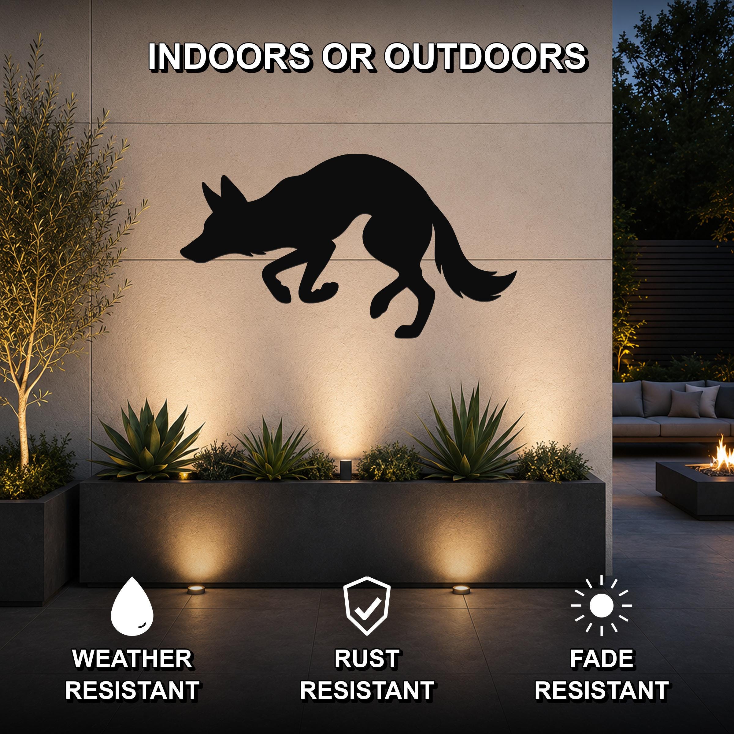 Black metal coyote wall art silhouette mounted on an outdoor patio wall above a planter, with text indicating it is weather, rust, and fade resistant for indoor or outdoor use.