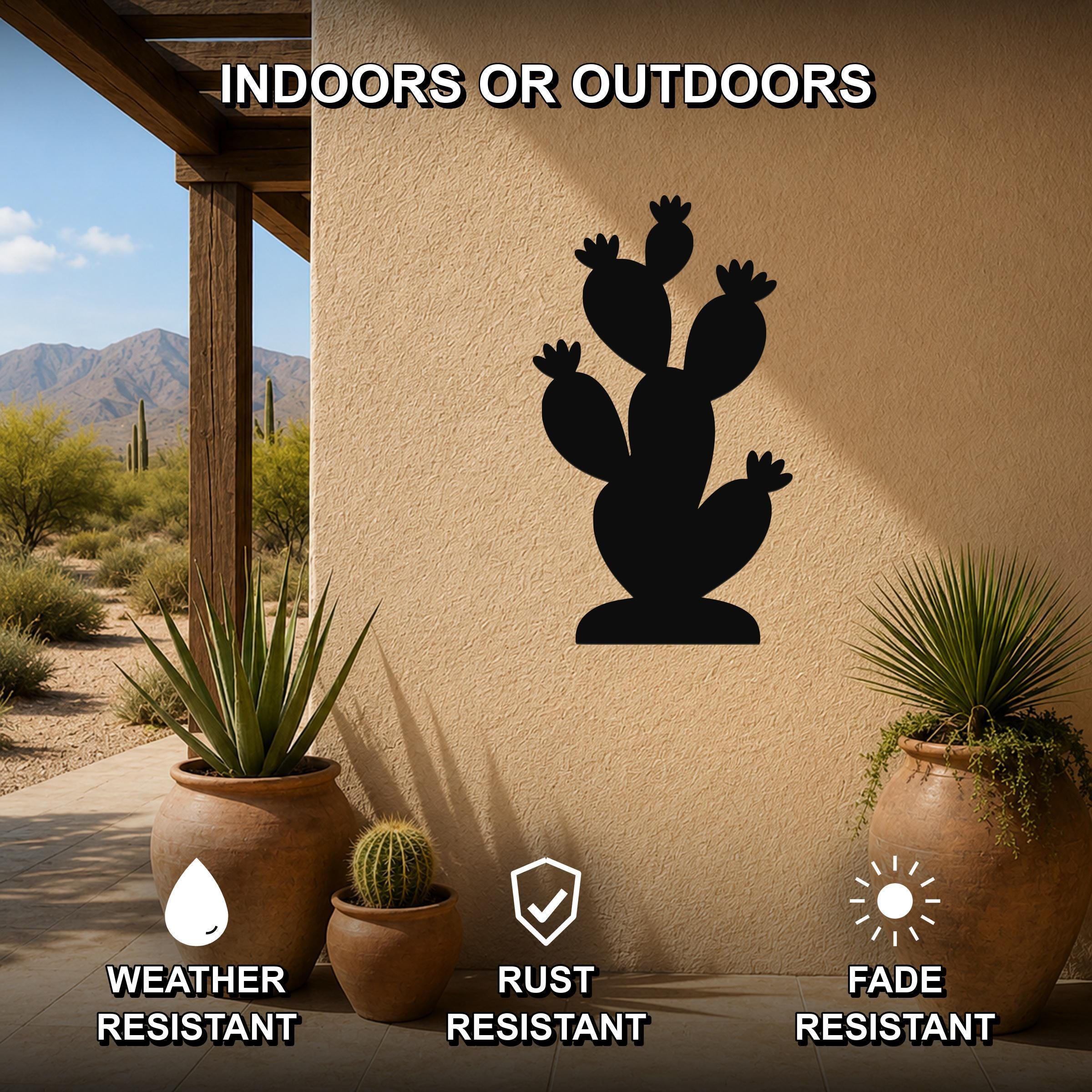 Black metal prickly pear cactus wall art silhouette mounted on a beige outdoor wall, displayed on a patio with potted plants and desert scenery in the background.