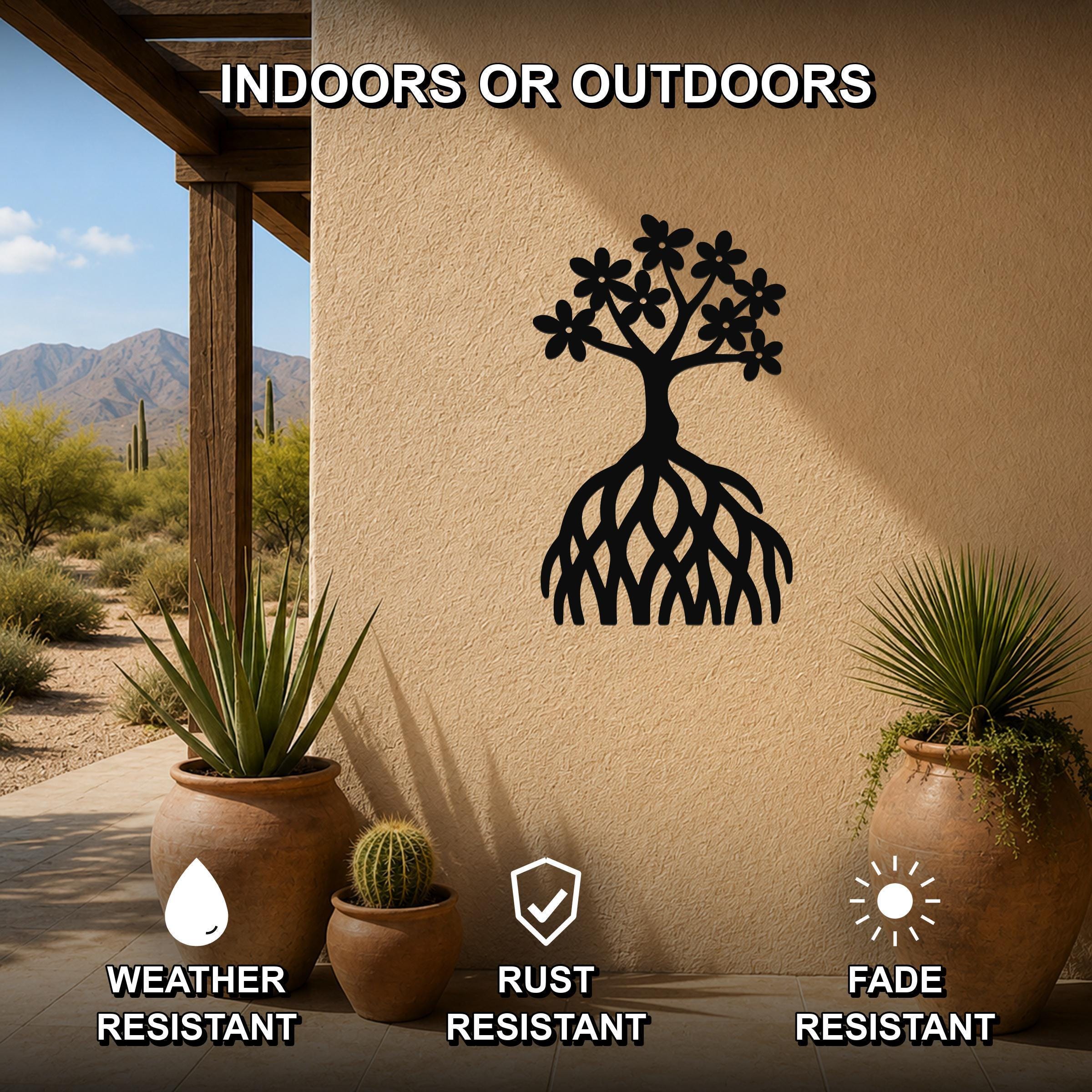 Black metal tree of life wall art with flower and root cutouts, mounted on an outdoor patio wall above potted plants.