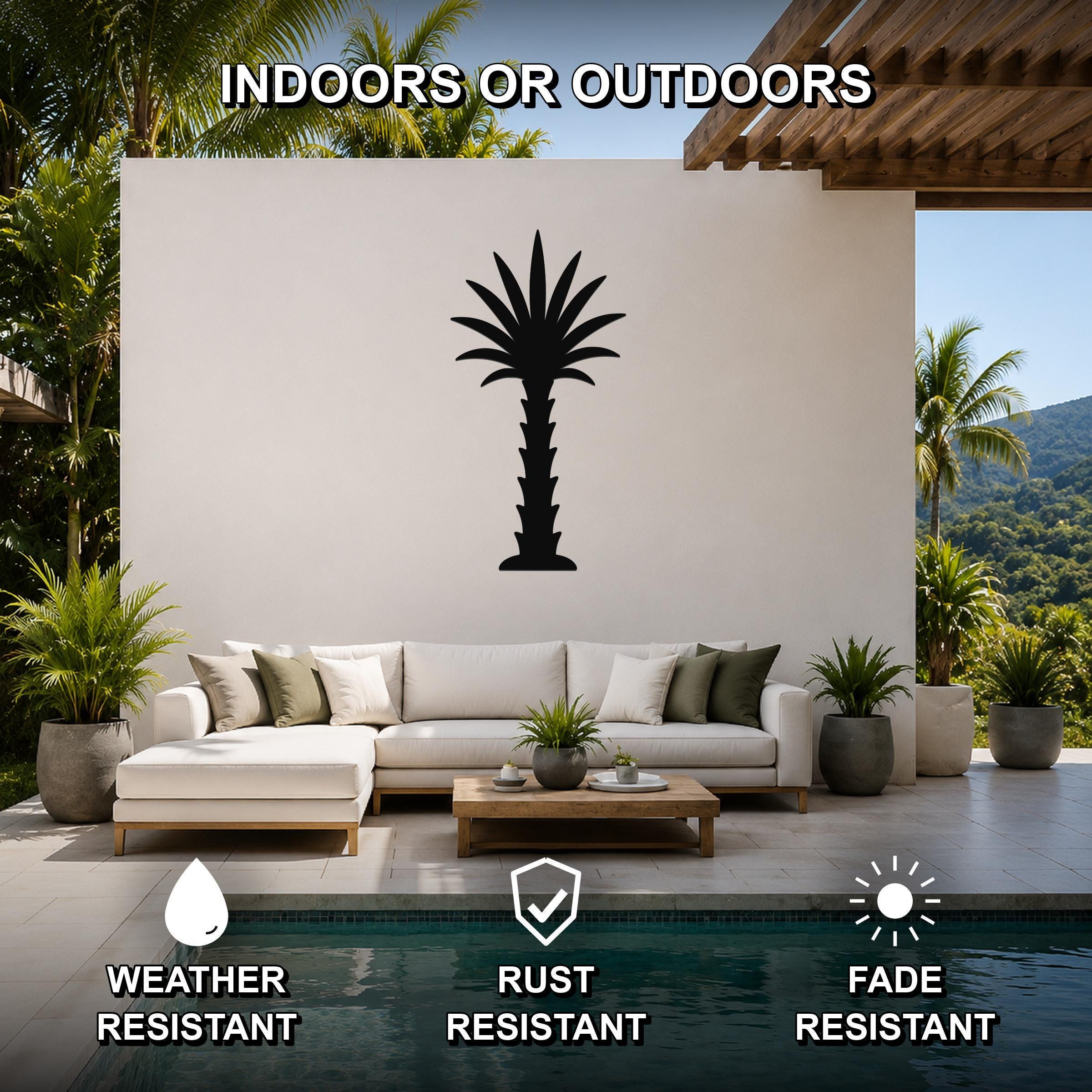 Black metal palm tree wall art silhouette mounted on a white outdoor wall above a sofa in a patio living area.