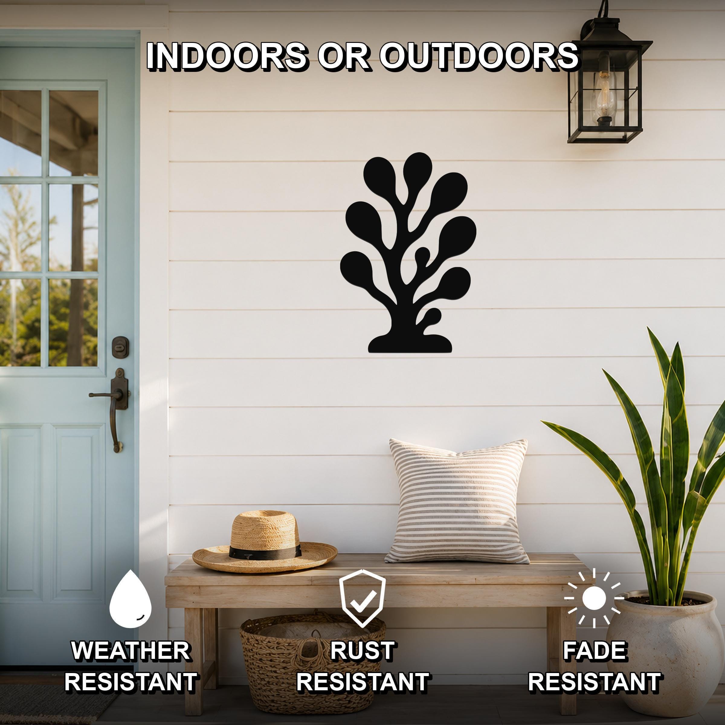 Black metal coral wall art with leafy cutout design, mounted on a white shiplap wall above a wooden bench on a porch.