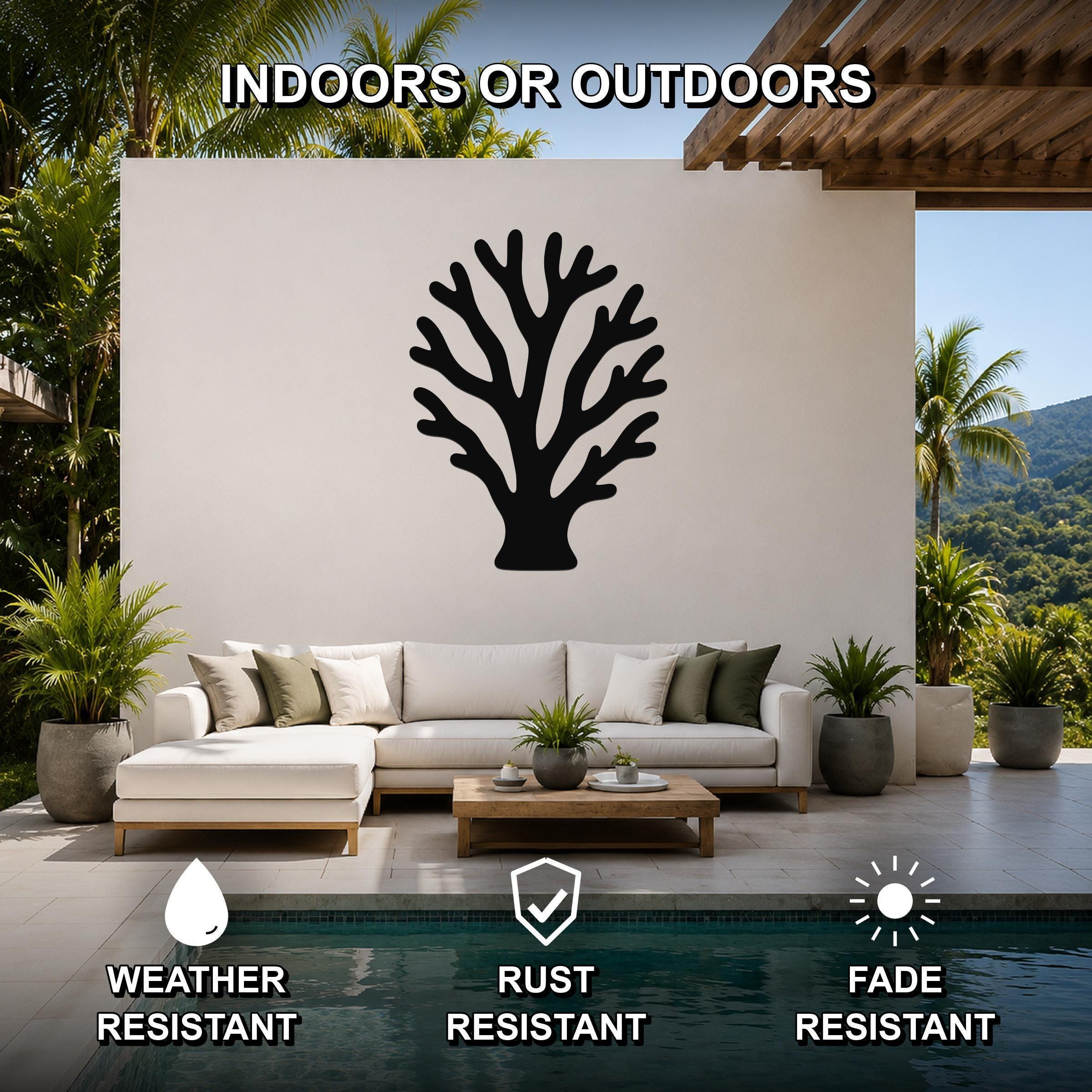 Black metal branching coral wall art with intricate cutout details, mounted on a white outdoor wall above a sofa in a patio living area.