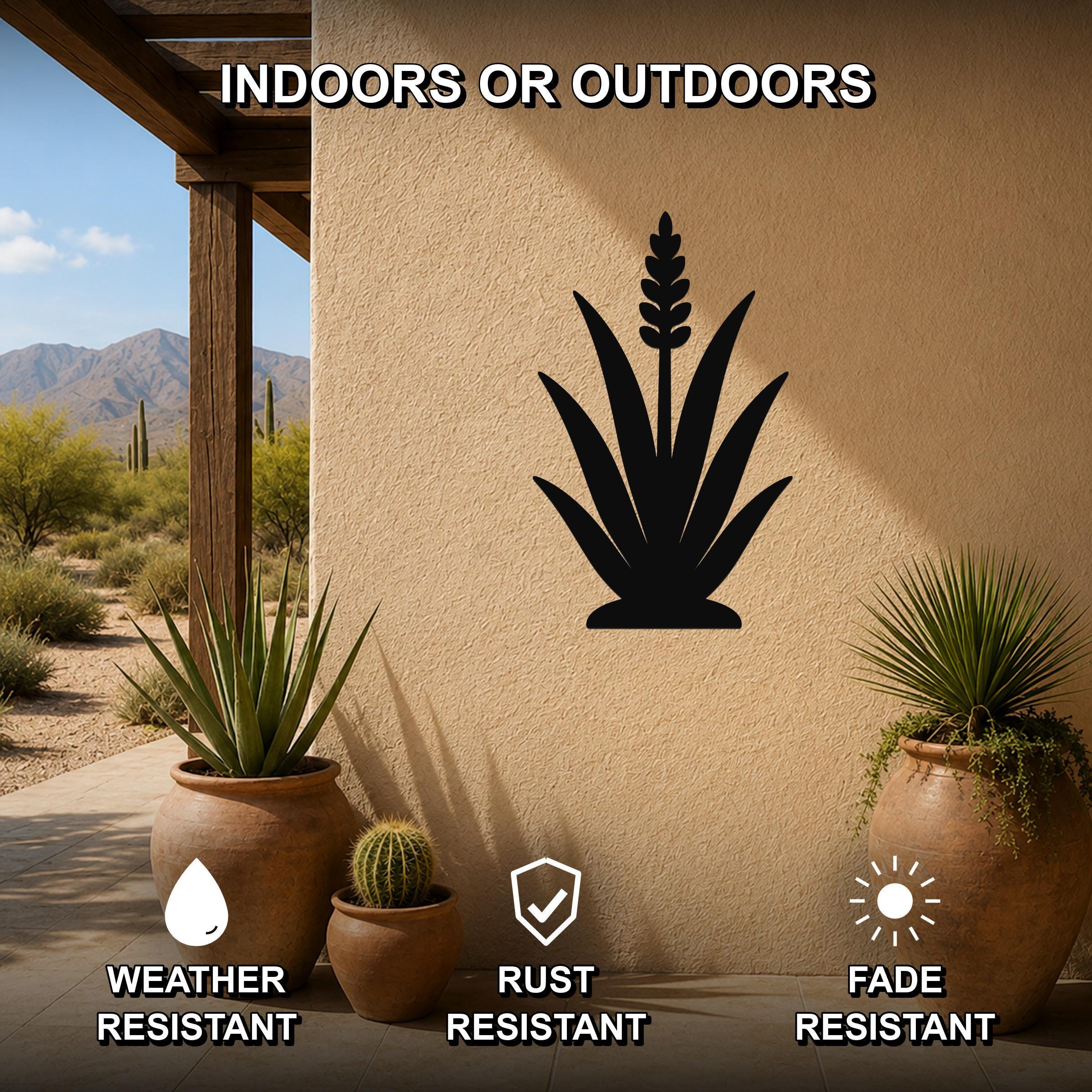 Black metal agave wall art silhouette mounted on a stucco outdoor wall, displayed on a patio with potted plants and desert scenery in the background.
