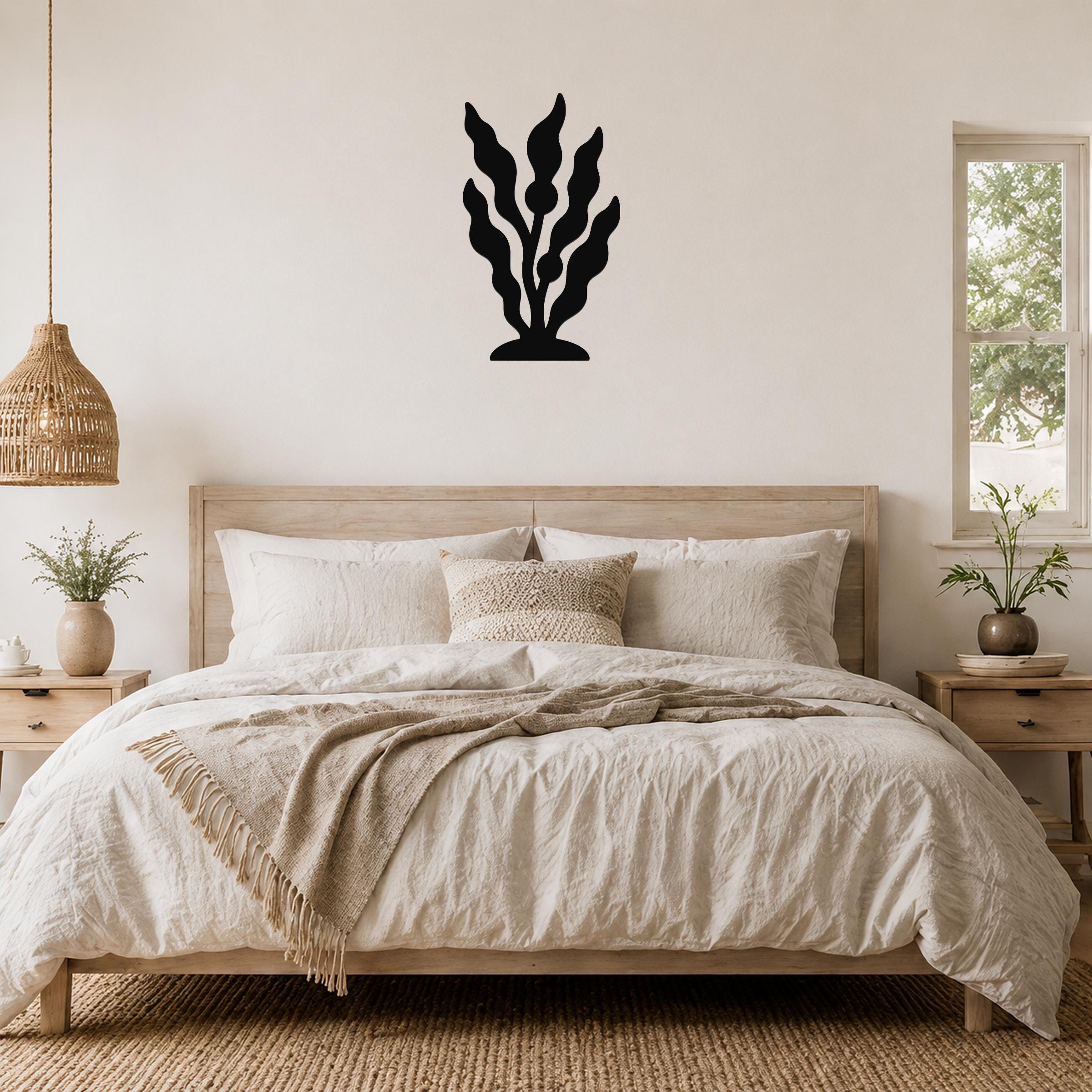 Black metal kelp wall art with flowing leaf cutouts, mounted above a wooden bed in a neutral bedroom.