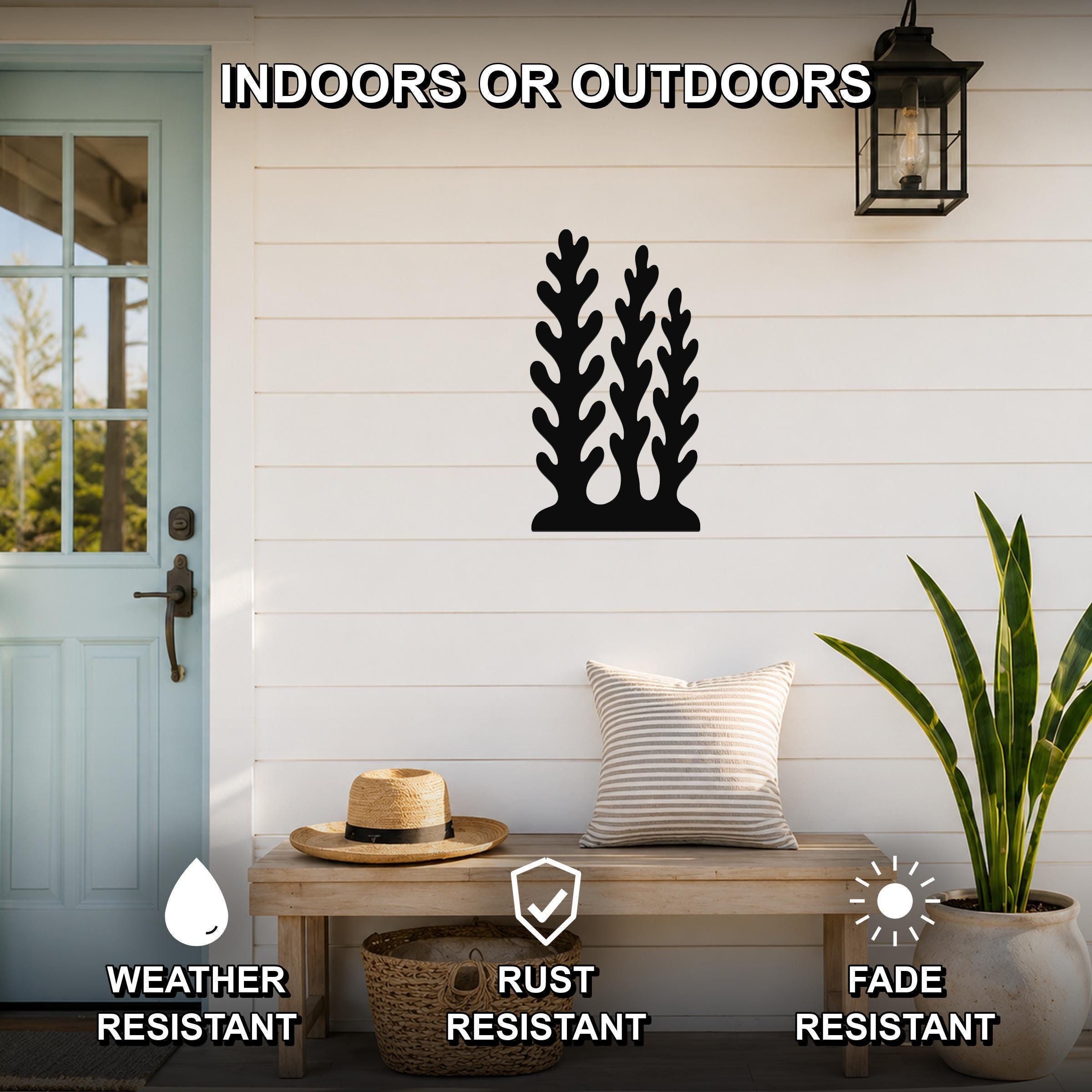 Black metal kelp and seaweed wall art with leafy cutouts, mounted on a white shiplap wall above a wooden bench on a porch.
