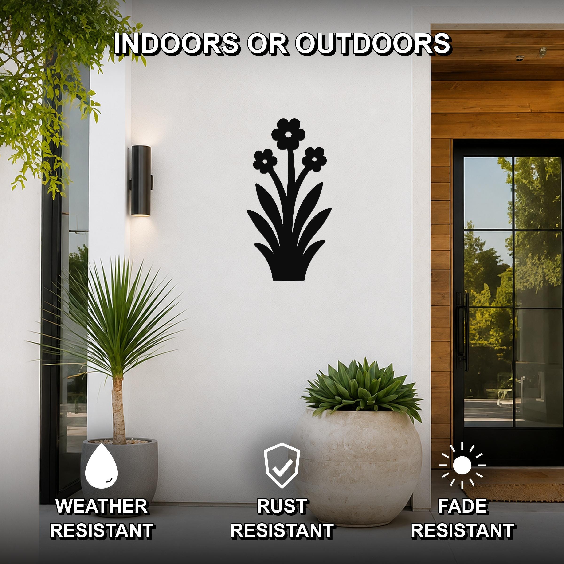 Black metal wildflower wall art with three flower cutouts and leafy stems, mounted on a white exterior wall beside a glass door and potted plants, suitable for indoor or outdoor use.