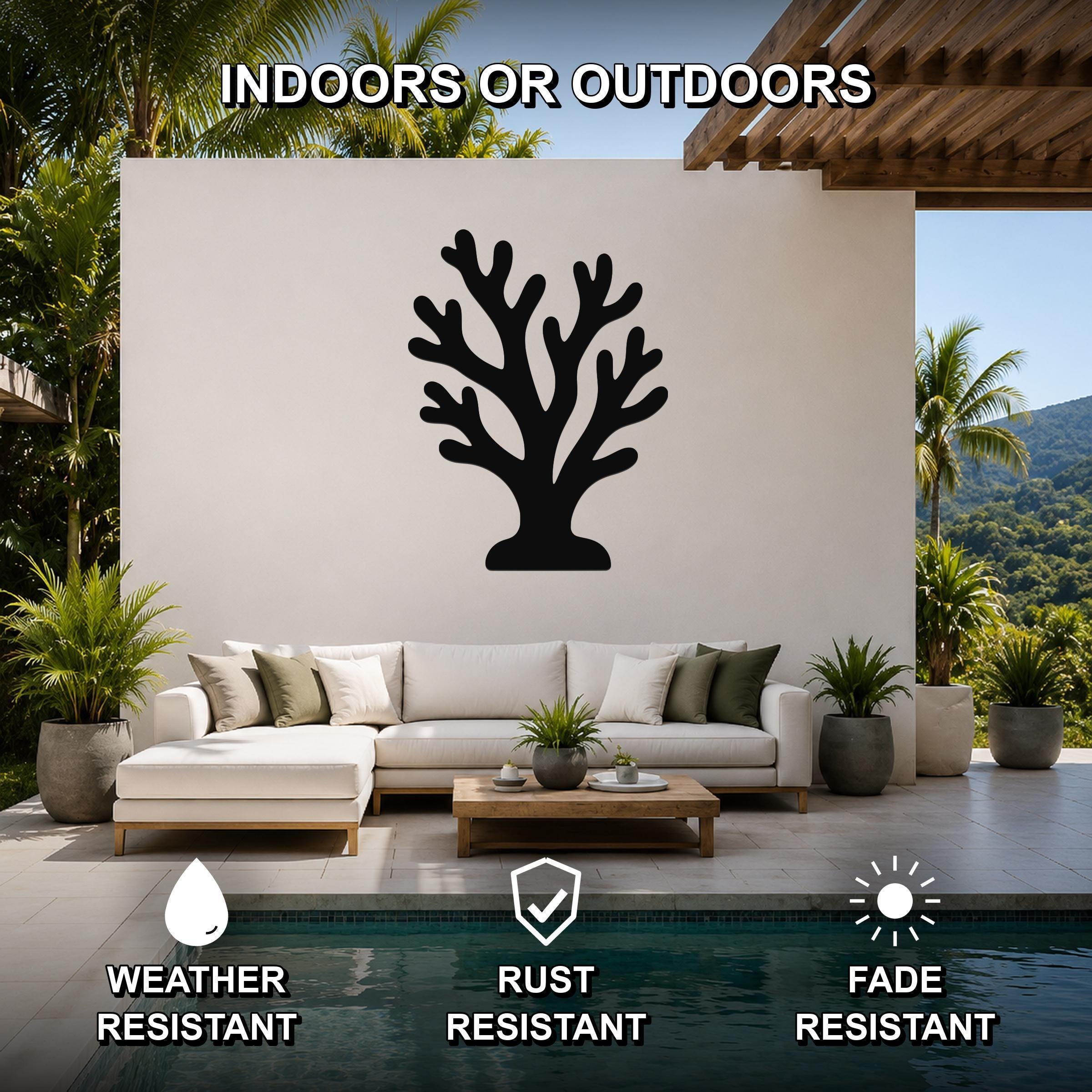 Black metal coral wall art with branching cutouts, mounted on a white outdoor wall above a sofa in a patio living area.