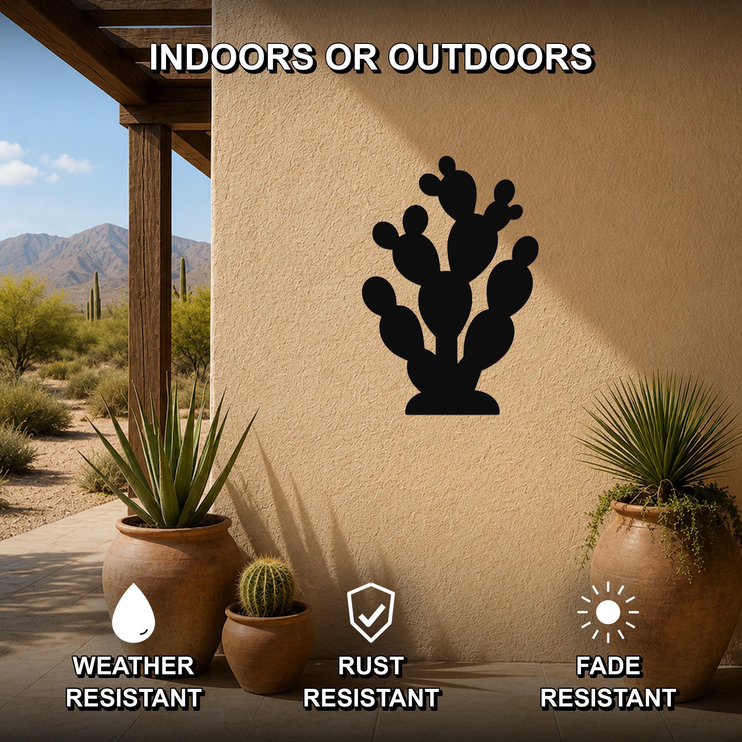 Black metal prickly pear cactus wall art silhouette mounted on a beige outdoor wall, displayed on a patio with potted plants and desert scenery in the background.