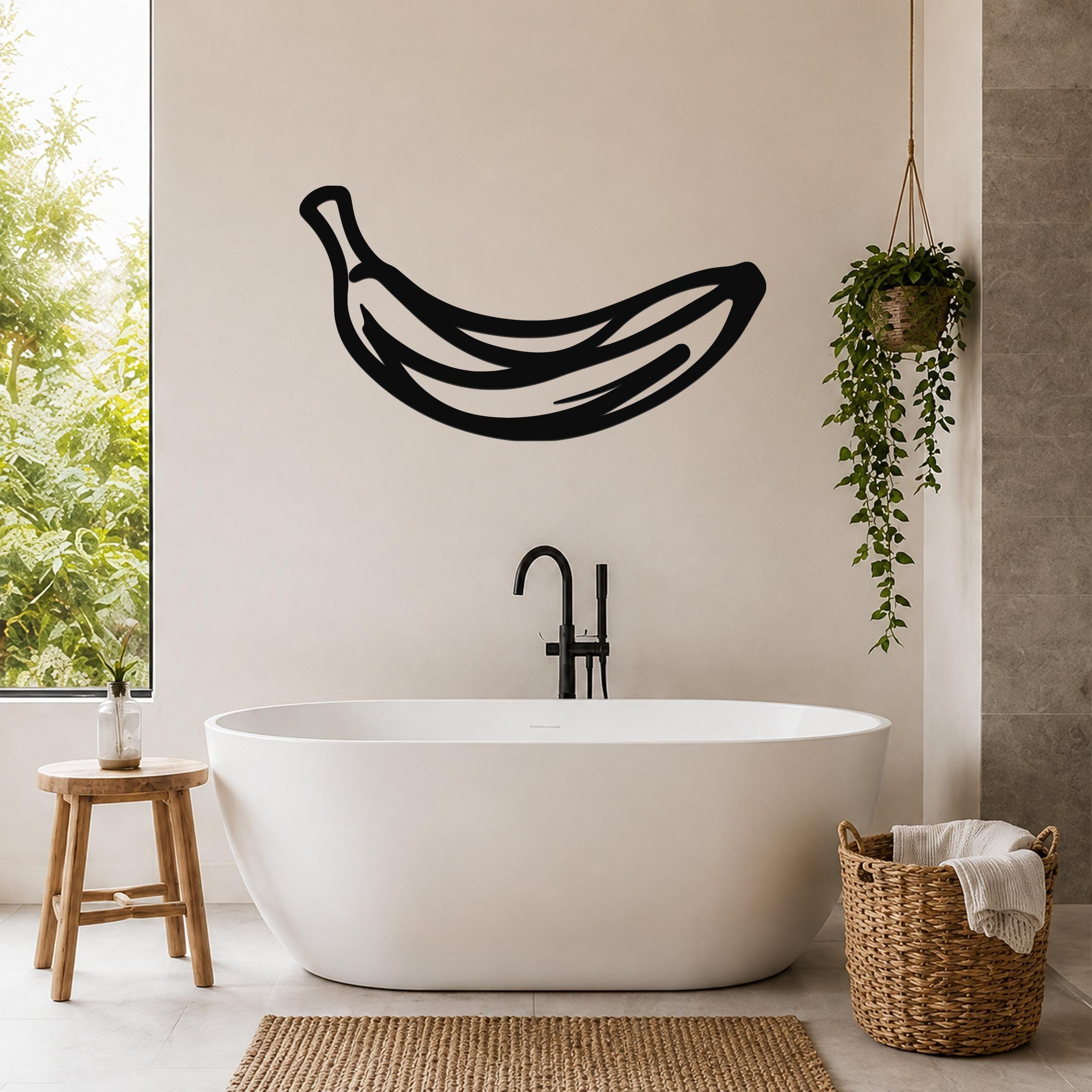 Black metal banana wall art with internal line cutouts, mounted on a bathroom wall above a freestanding tub.