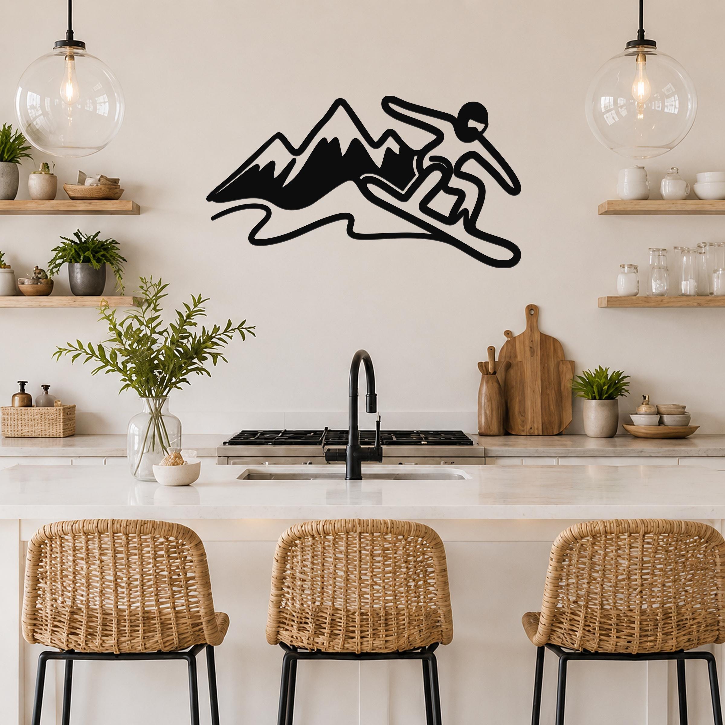 Black metal wall art silhouette of a snowboarder in motion above a kitchen counter, mounted on a light-colored wall between two glass pendant lights.