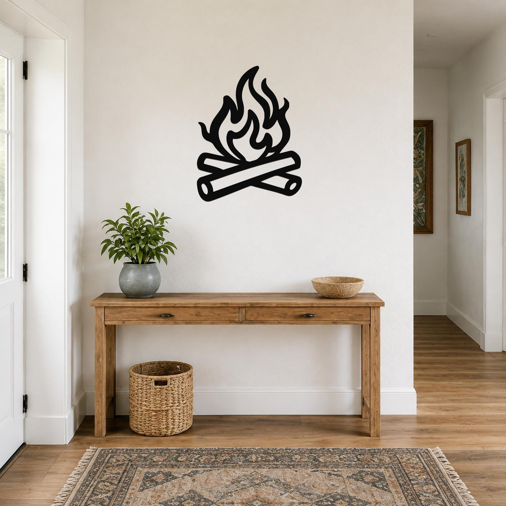 Black metal campfire wall art with flame and log silhouette, mounted on a white wall above a wooden console table in a hallway.